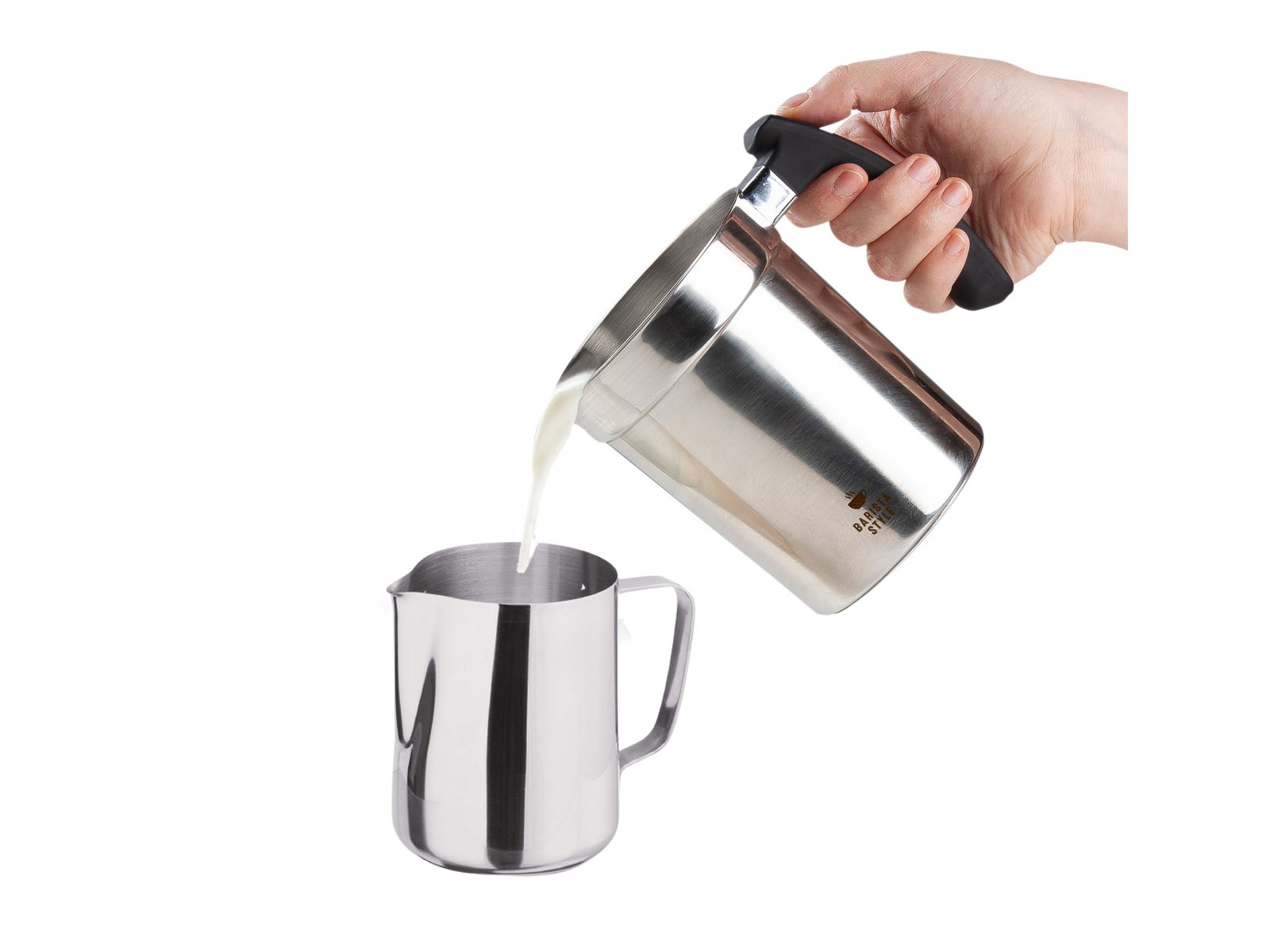 Eine Hand gießt Milch aus einem Metallkrug in einen kleineren Metallkrug.