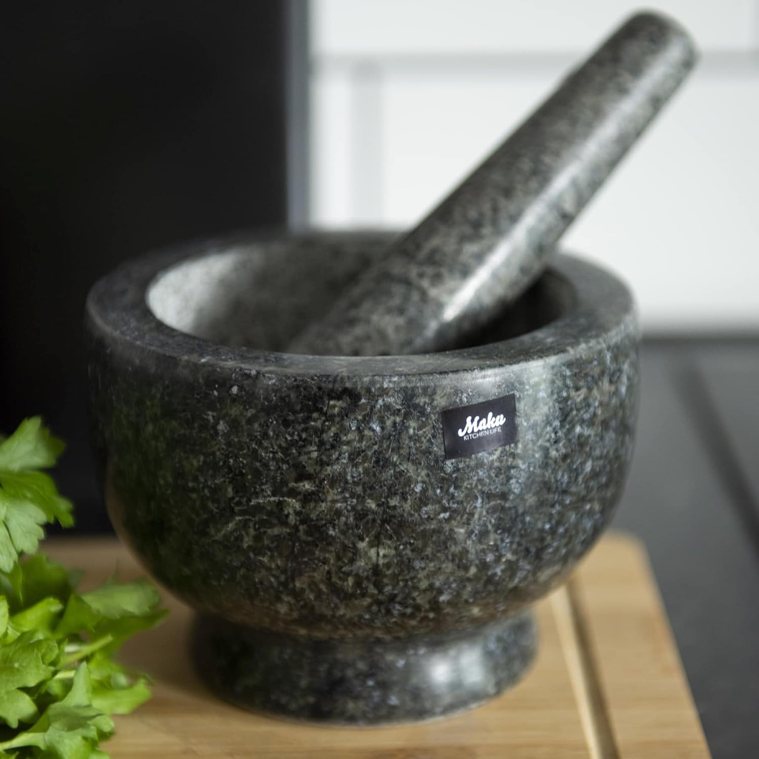 Ein Granit-Mörser und Stößel auf einem Holzbrett mit Petersilie. Der Mörser hat ein Etikett.