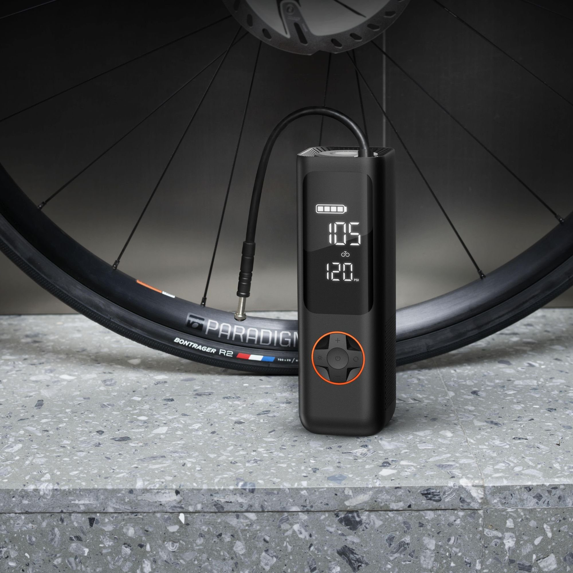 Schwarzer Fahrradreifen-Inflator mit Digitalanzeige und Knöpfen. Ein Fahrradrad im Hintergrund.