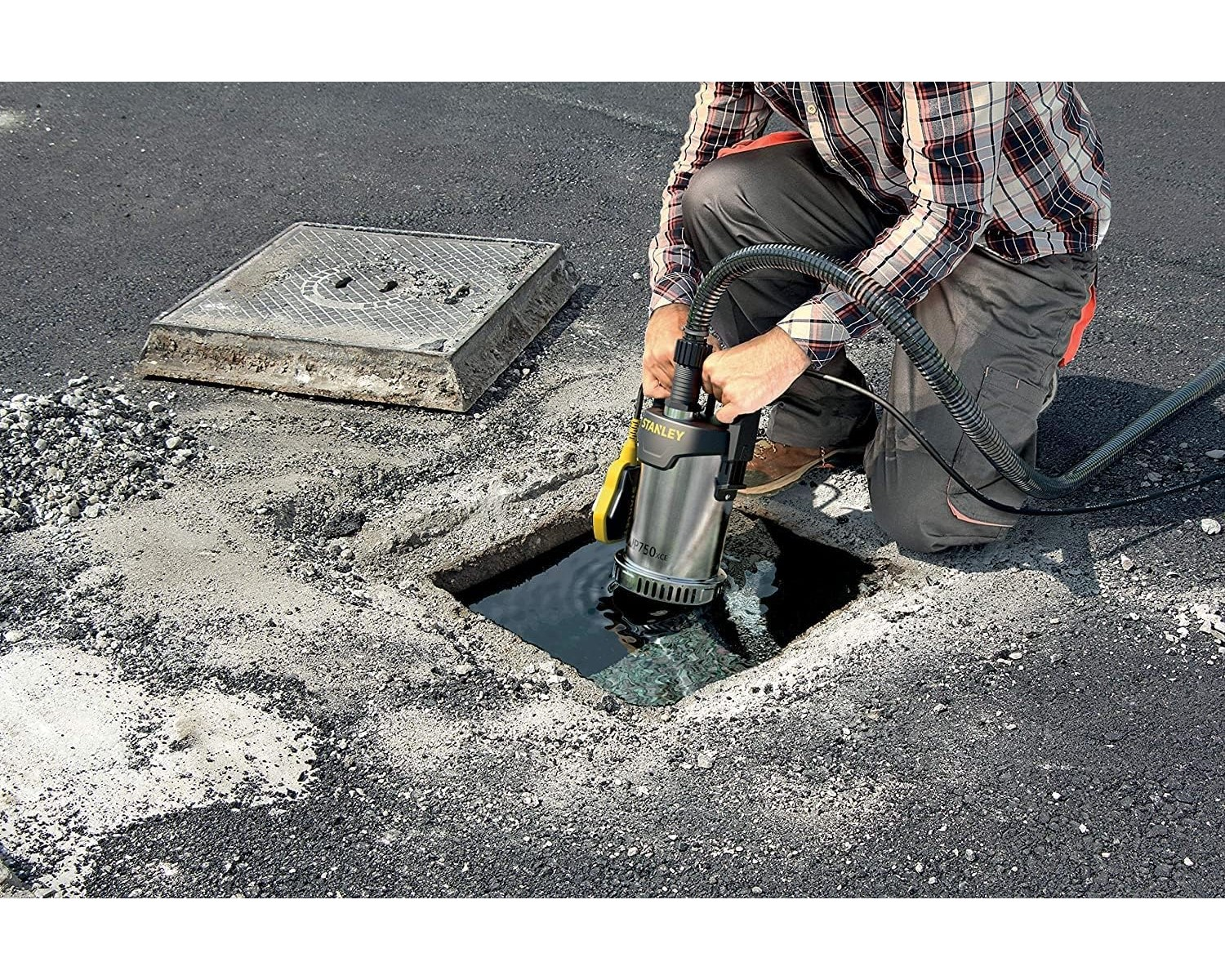 Eine Person pumpt Wasser aus einem quadratischen Loch in Asphalt. Eine Stanley-Pumpe wird verwendet.