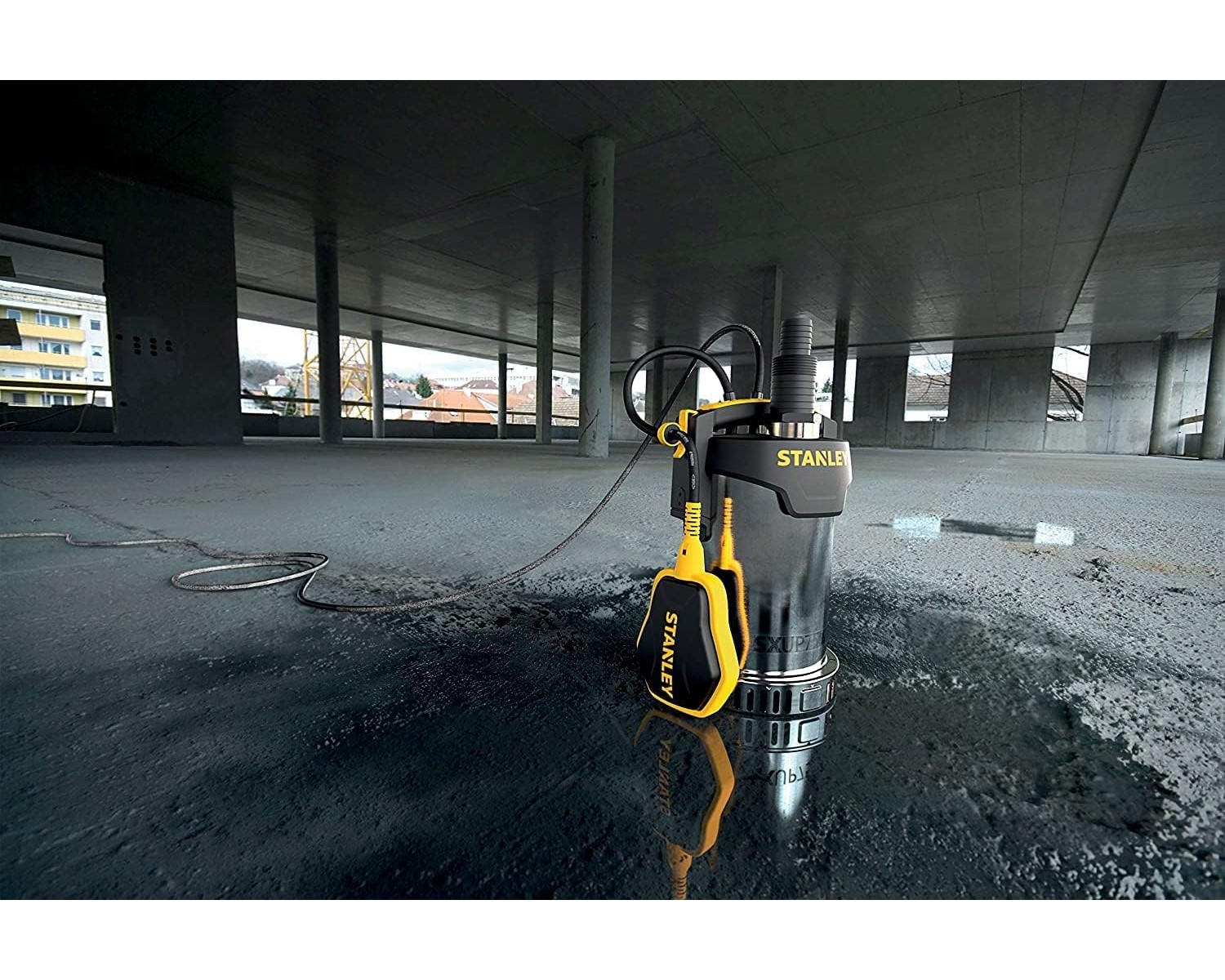 Schwarz-gelbe STANLEY Tauchpumpe. Auf Betonboden, mit Baustellenhintergrund platziert.