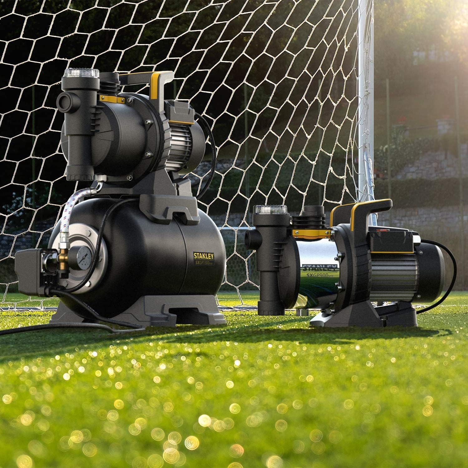 Zwei schwarz-gelbe Wasserpumpen auf grünem Feld, Fussballtor im Hintergrund.