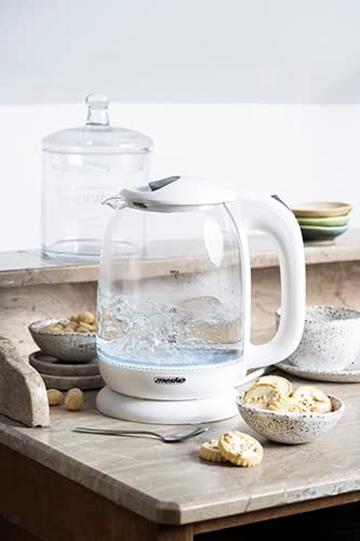 Un bollitore elettrico in vetro trasparente con acqua bollente e biscotti.