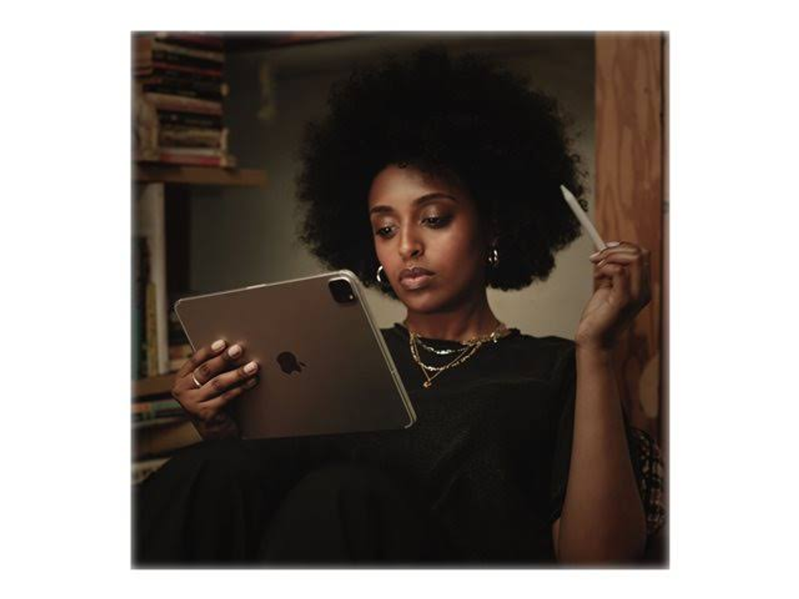 Eine Frau mit Afro sitzt und benutzt ein Tablet mit Stift. Bücherregale sind im Hintergrund.