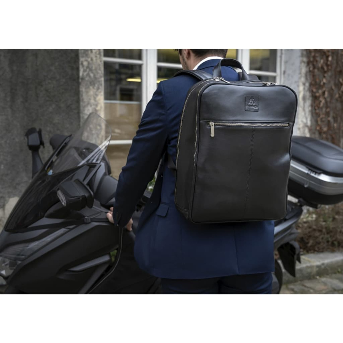 Hombre con mochila negra, traje azul, cerca de una moto. Toma exterior.