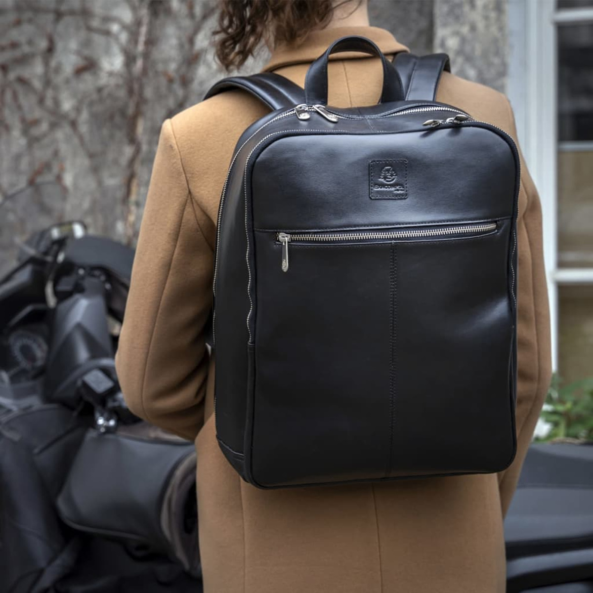 Una persona con una mochila de cuero negro, caminando cerca de una motocicleta.