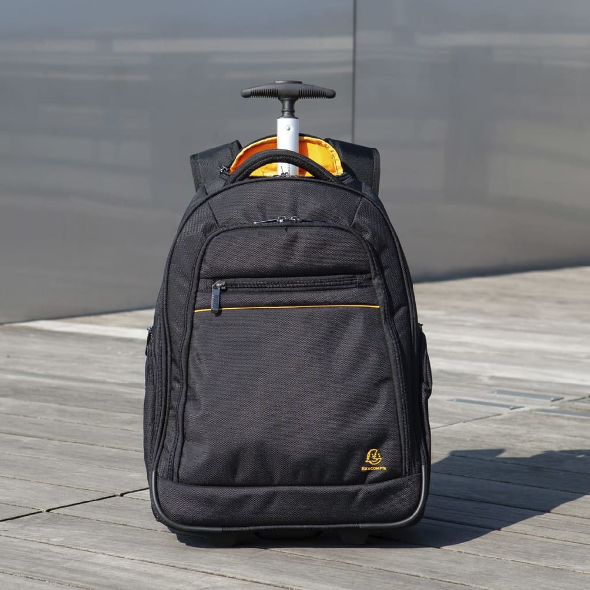 Mochila rodante negra sobre una superficie de madera. Tiene interior amarillo, ribetes naranjas y un asa.