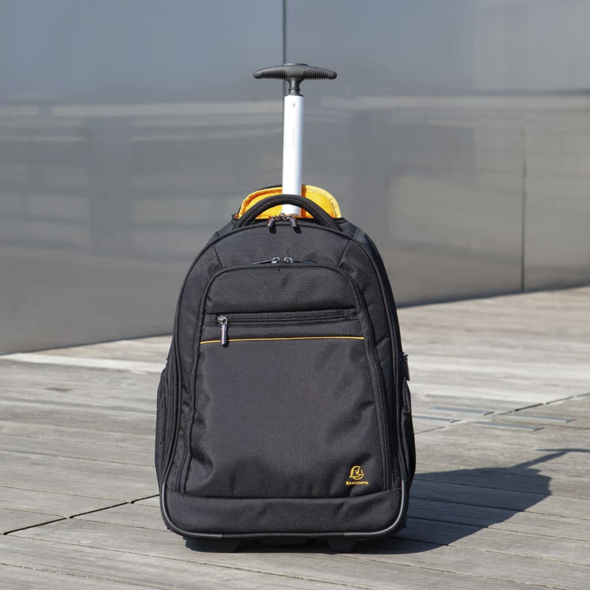 Mochila rodante negra con asa extendida, sobre superficie de madera al aire libre.