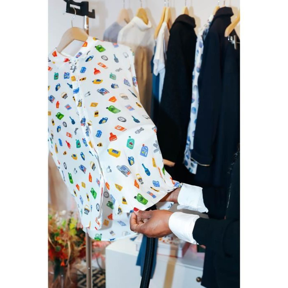 Donna che tiene in mano una camicia con un motivo colorato di icone, vestiti su un rack.