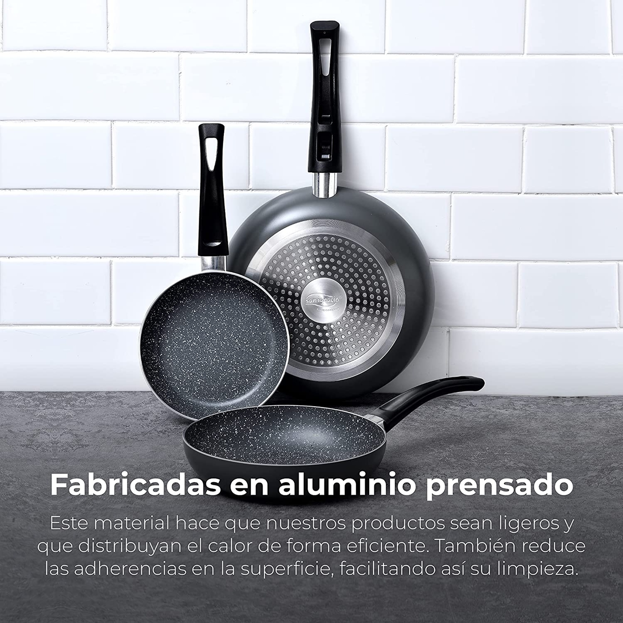 Tres sartenes con mangos negros dispuestas sobre un fondo de azulejos blancos.