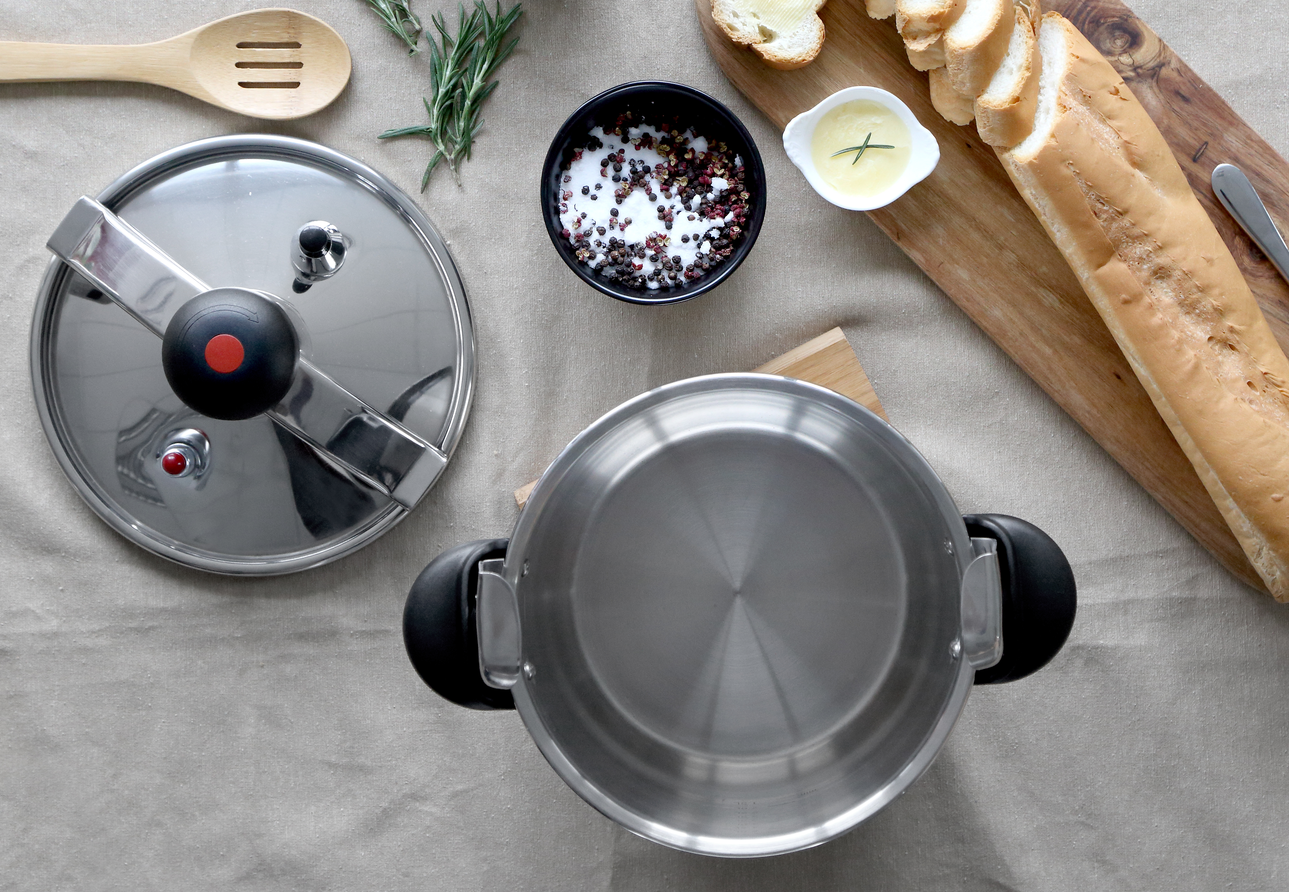 Vista superior de una olla a presión de acero inoxidable con tapa, hierbas e ingredientes en una mesa.