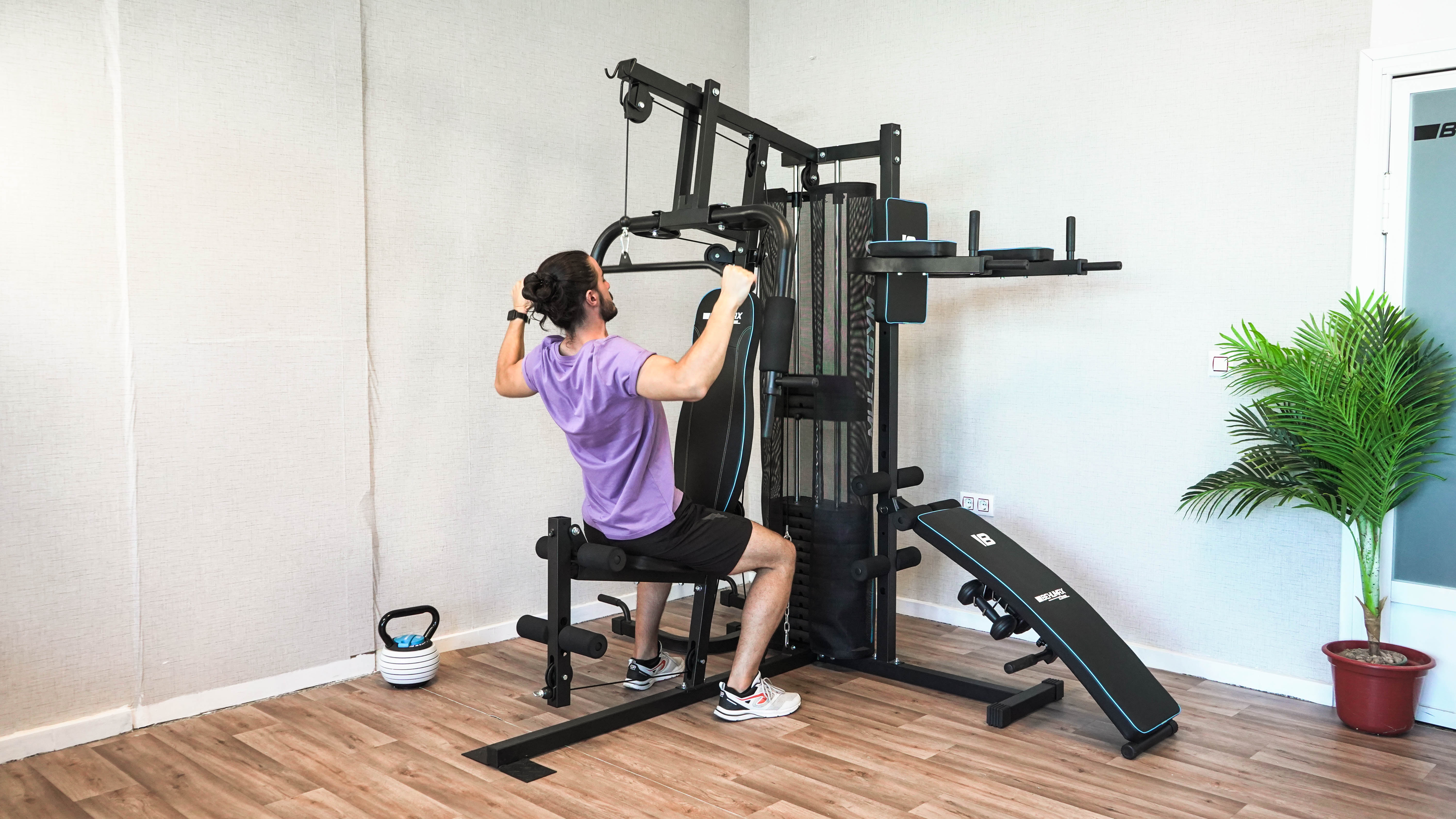 Hombre haciendo ejercicio en un gimnasio en casa negro. Banco y pesa rusa visibles.