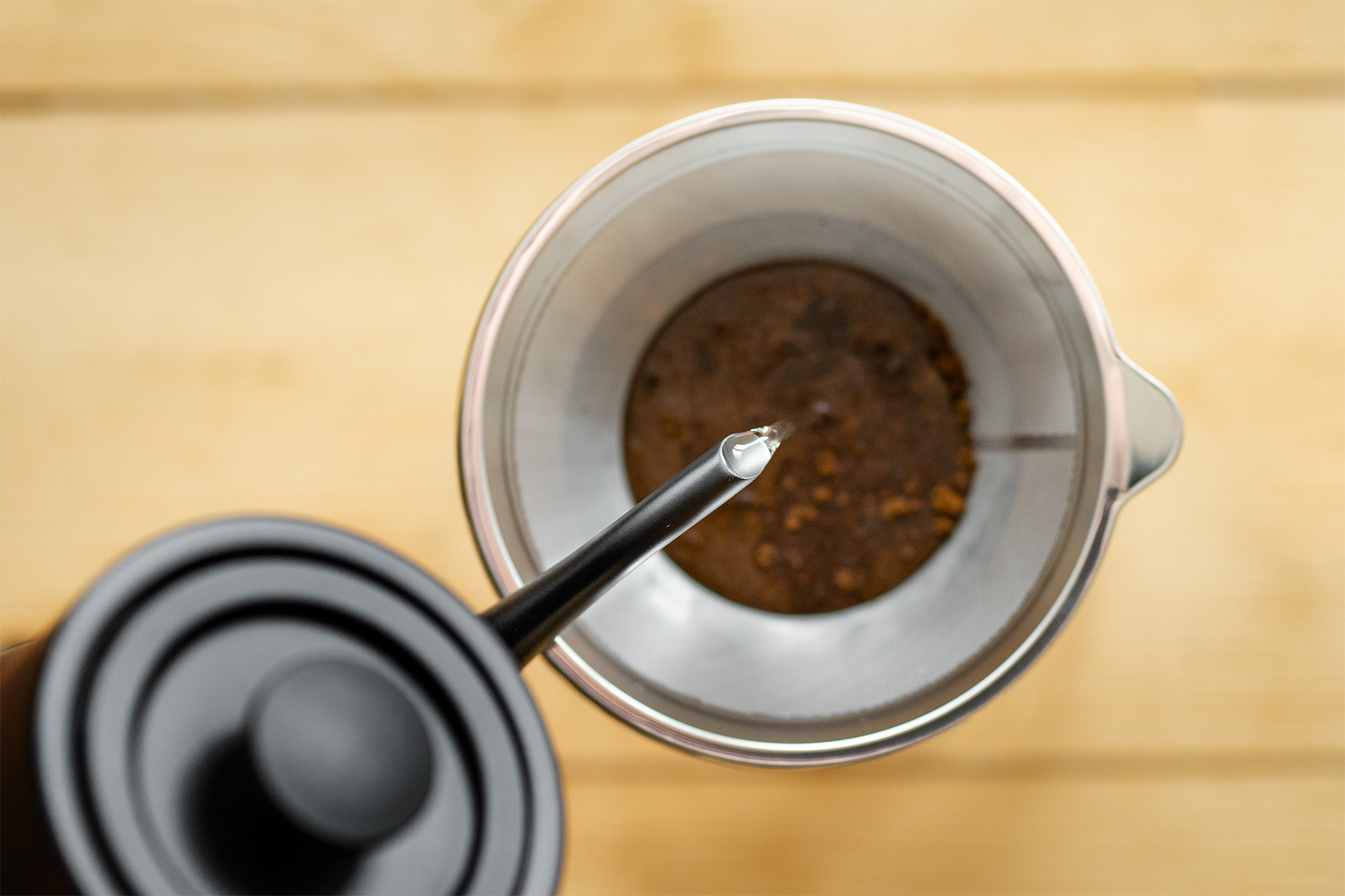 Eine Draufsicht auf Kaffee, der aus einem schwarzen Schwanenhalskessel in einen Filter gegossen wird.