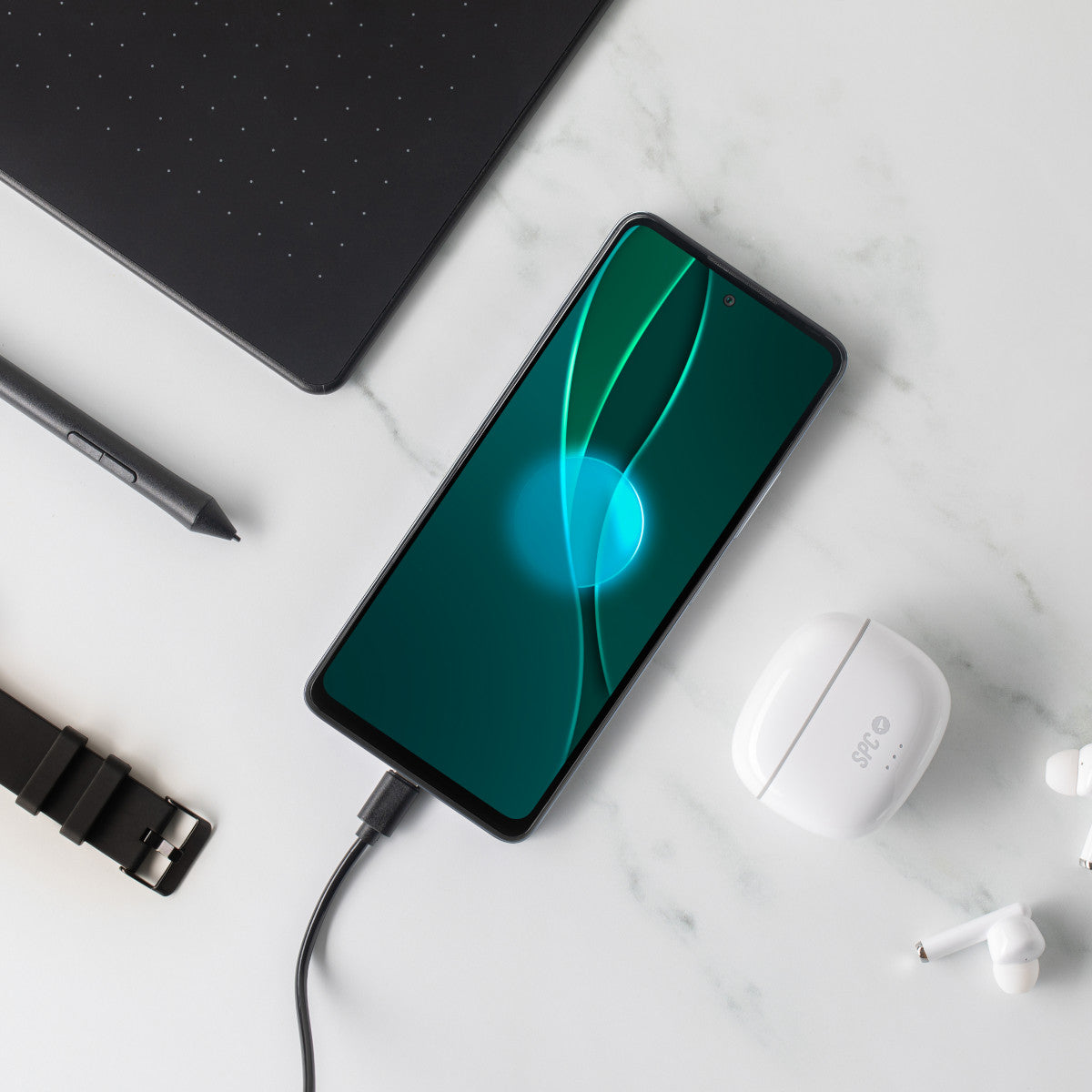 Un telefono in carica su una superficie bianca, accanto a auricolari e un tablet.