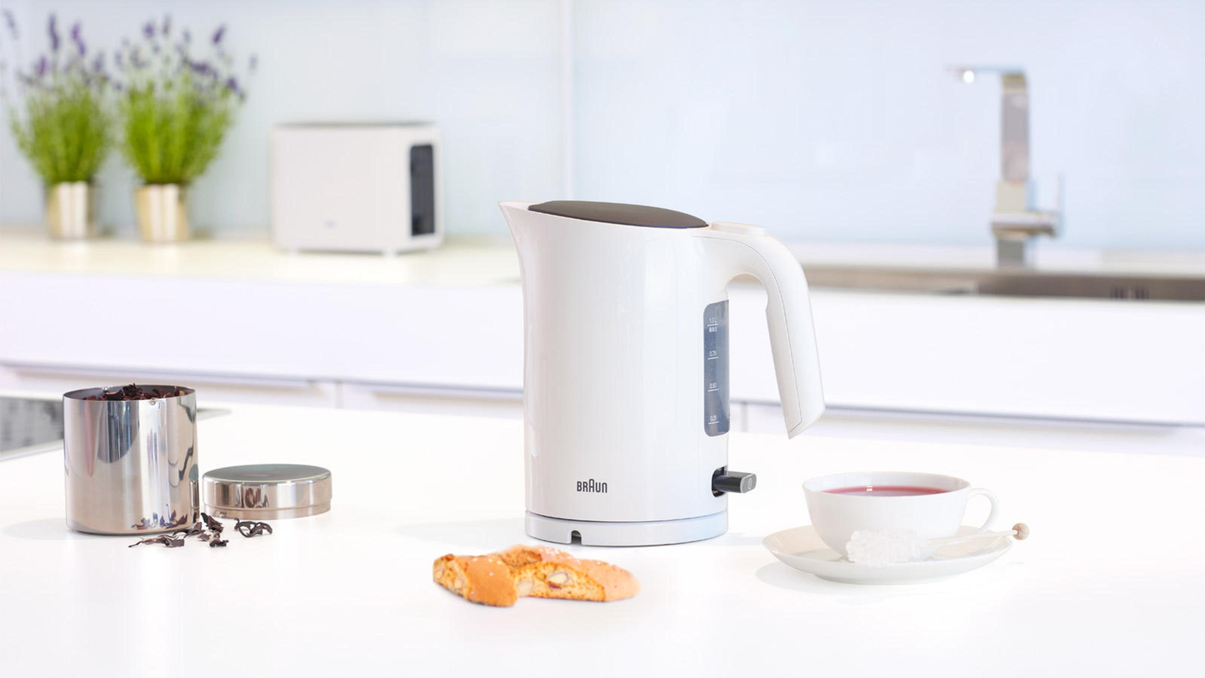 Weißer Wasserkocher auf weißer Oberfläche, mit Tasse und Biscotti.
