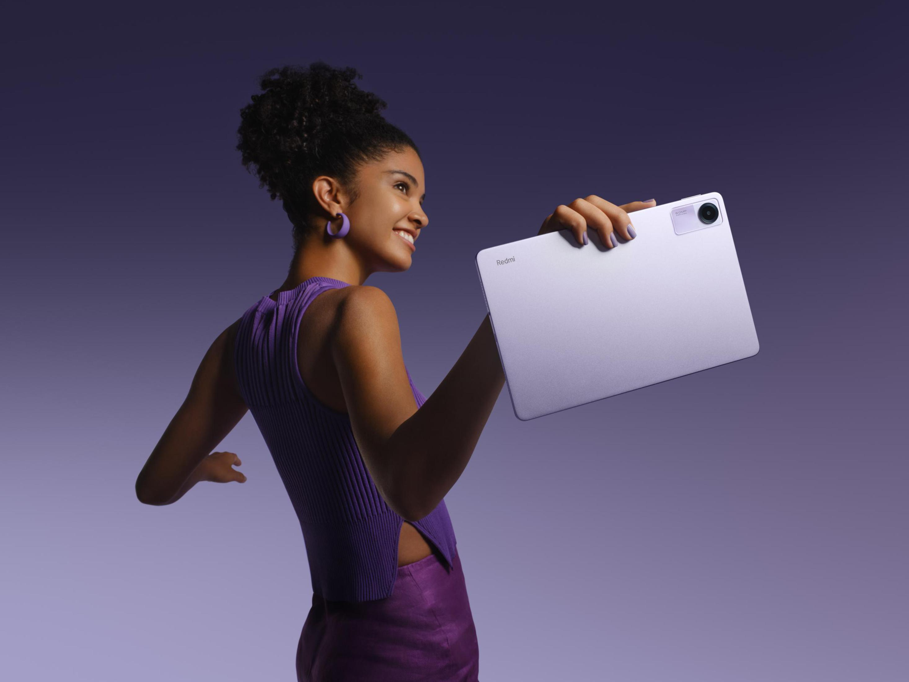 Kobieta trzymająca tablet. Uśmiecha się z fioletowymi dodatkami i ubraniami, fioletowe tło.