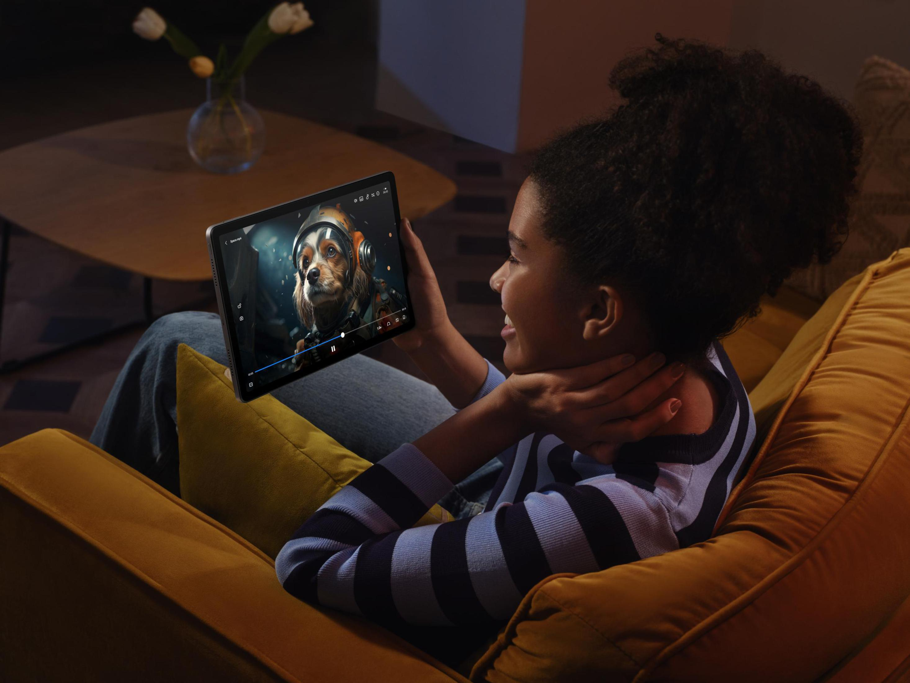 Una niña sonriendo mientras ve una película en una tableta. Hay una imagen de un perro en la pantalla.