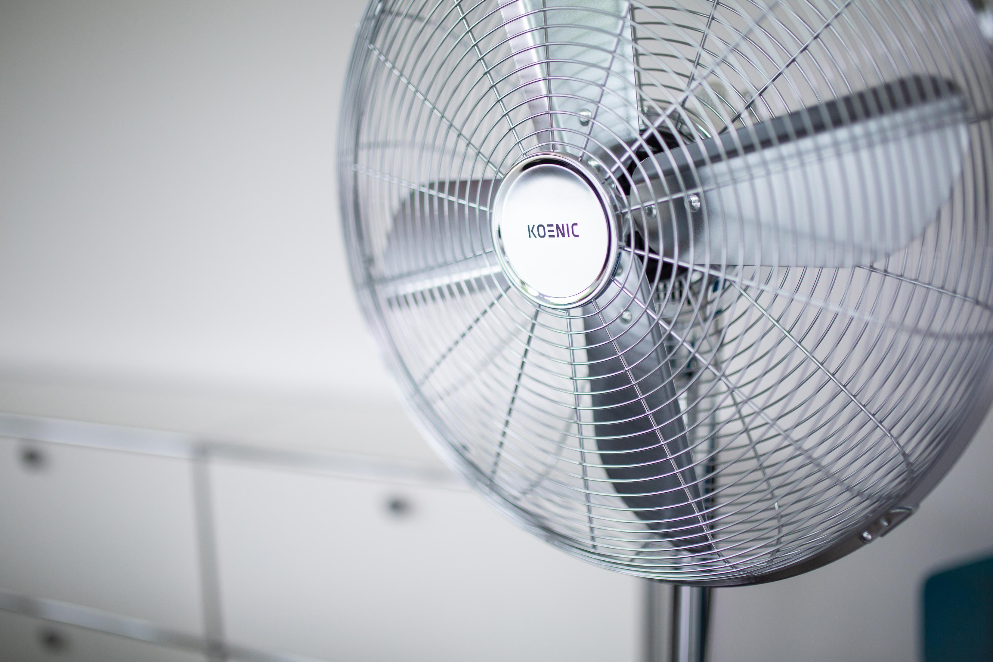 Silberner Koenic-Ventilator auf weißem Hintergrund. Der Ventilator ist eingeschaltet, die Blätter sind sichtbar.