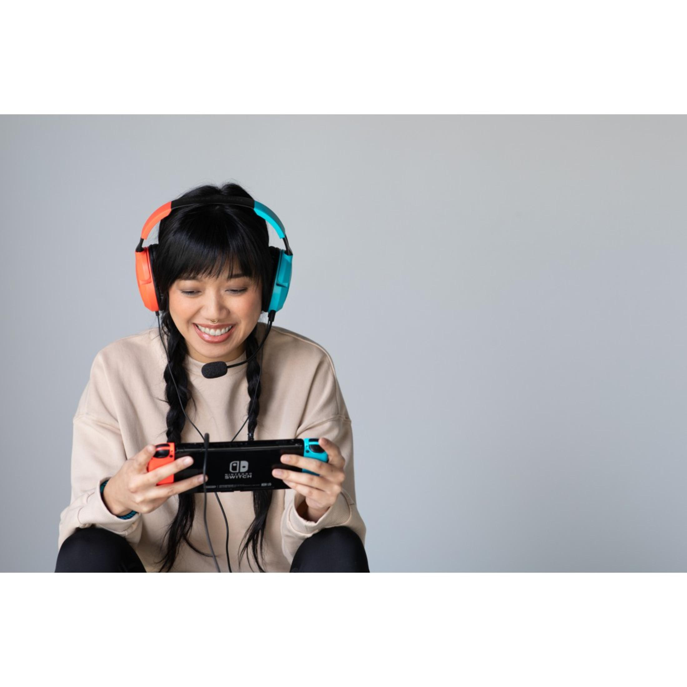 Młoda kobieta uśmiecha się, nosząc zestaw słuchawkowy do gier i trzymając konsolę do gier z kontrolerami.