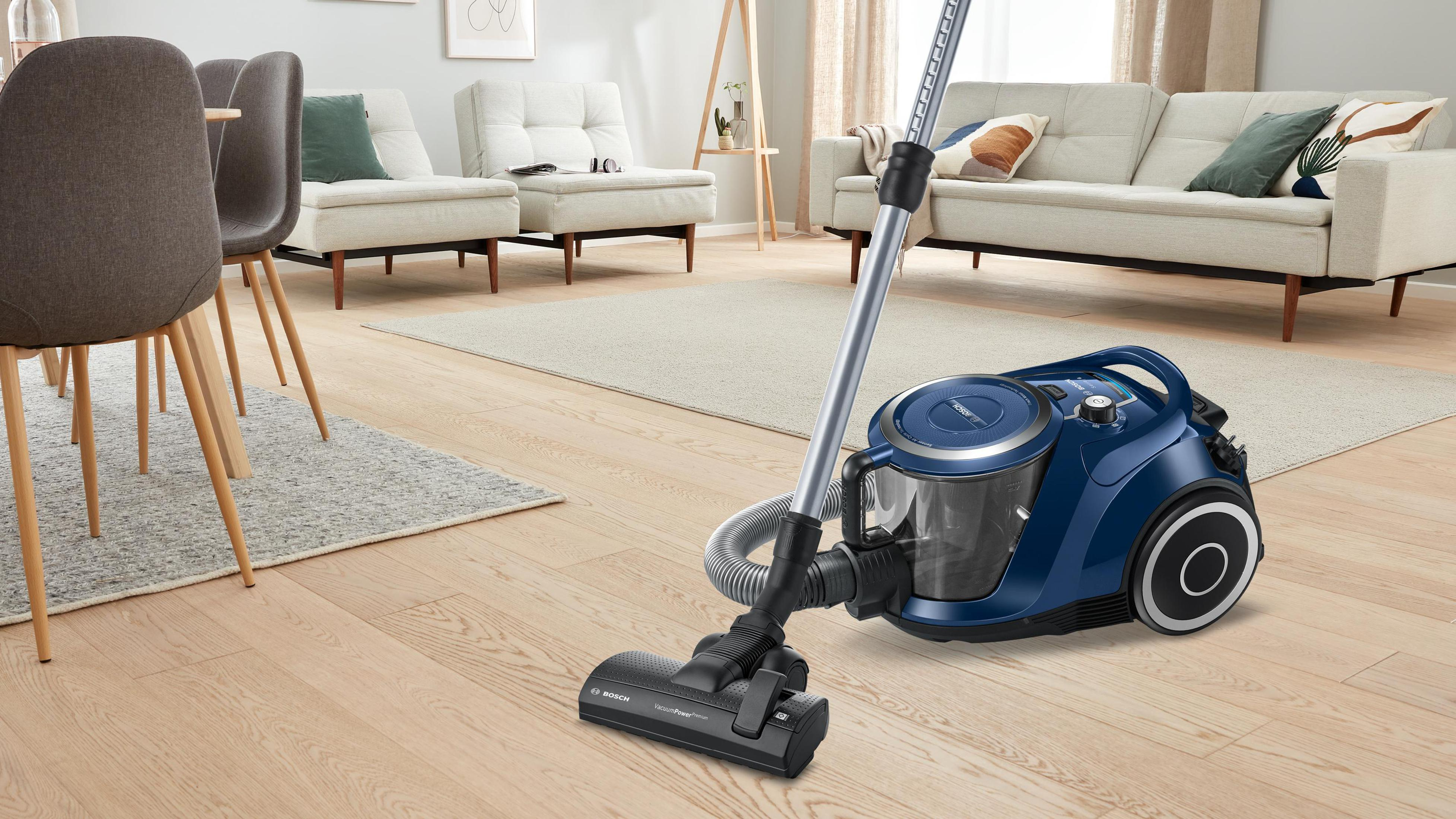 Niebieski odkurzacz w salonie z drewnianymi podłogami. Meble w tle.