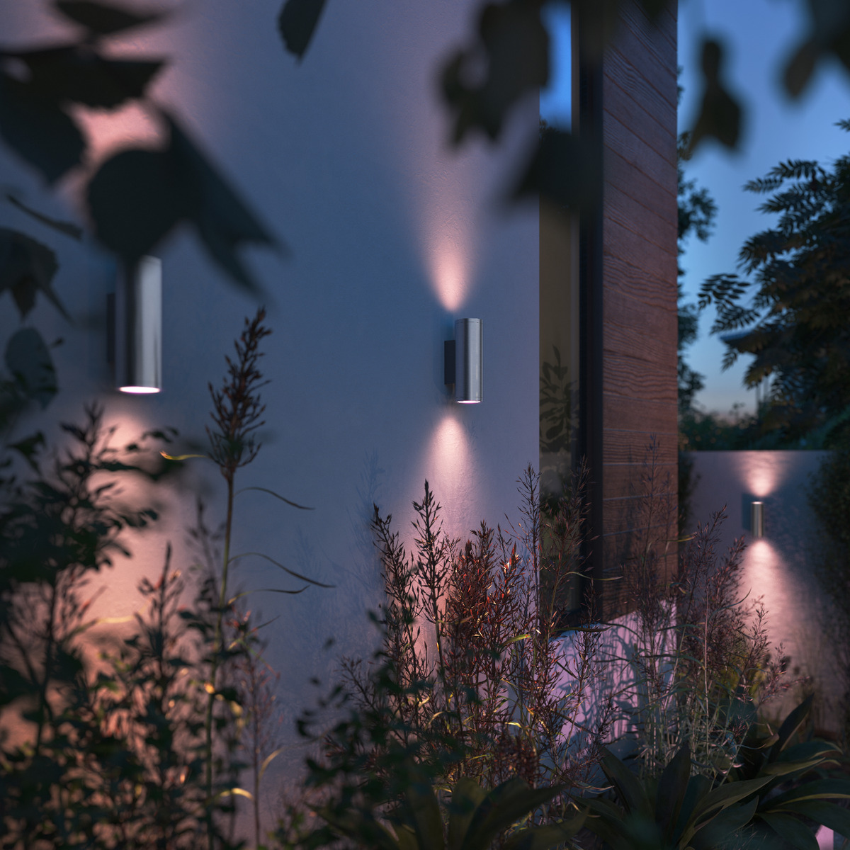 Zewnętrzne lampy ścienne oświetlają ścianę z roślinami z przodu. Światła są srebrne.