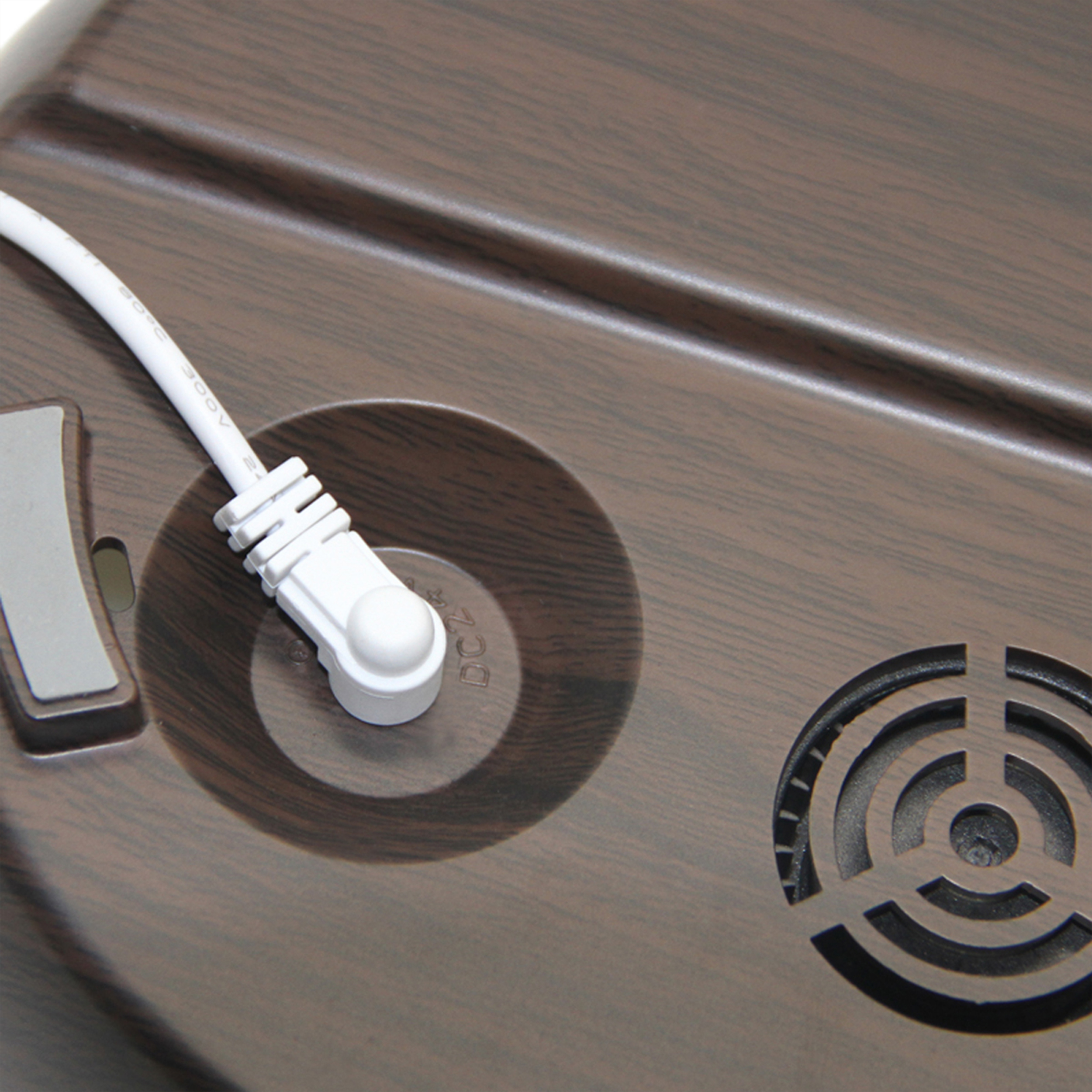 Zbliżenie drewnianej powierzchni z białym kablem wpiętym w okrągłe gniazdo. Widoczny wentylator.