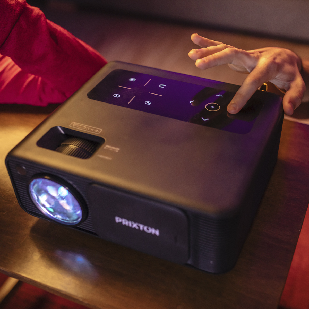 Czarny projektor na drewnianym stole, z ręką naciskającą przycisk na panelu sterowania.