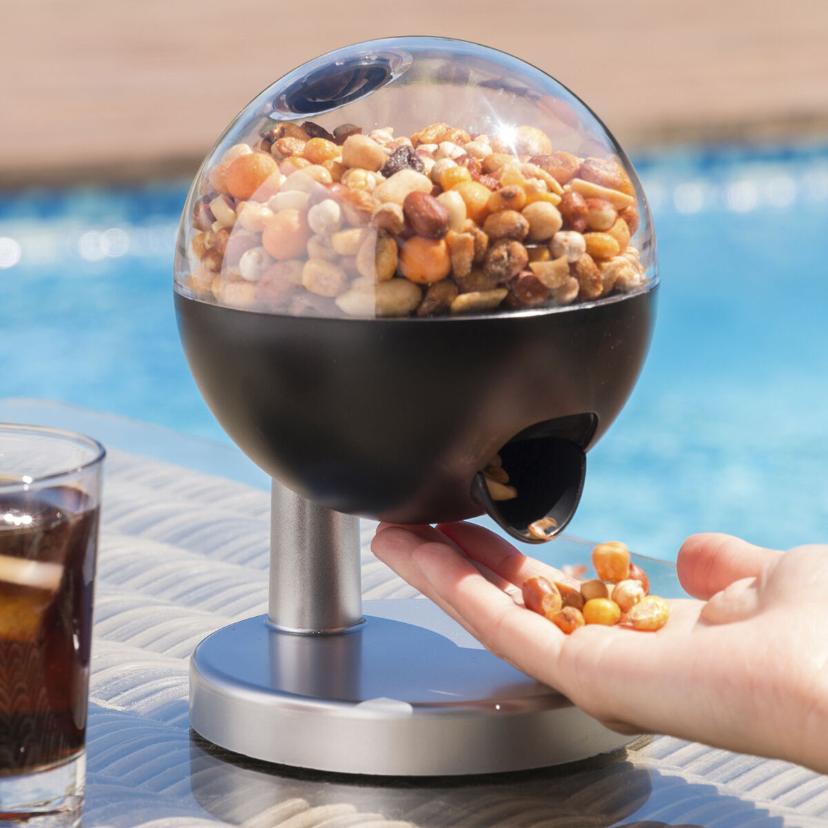 Un distributore a sfera trasparente pieno di noci. Una mano che prende le noci vicino a una piscina.