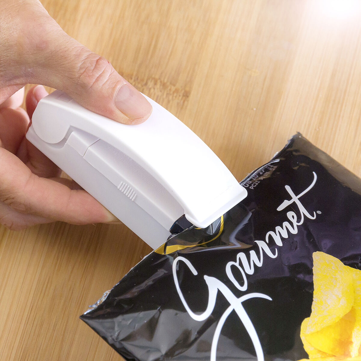 Die Hand einer Person verschließt eine schwarz-goldene Chipstüte mit einem weißen Versiegeler.
