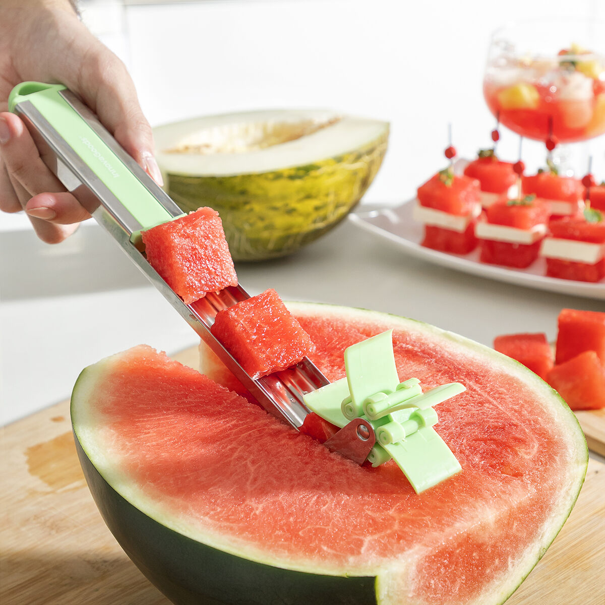 Eine Person schneidet Wassermelone mit einem grünen Werkzeug und einige Wassermelonenwürfel auf einem Teller.