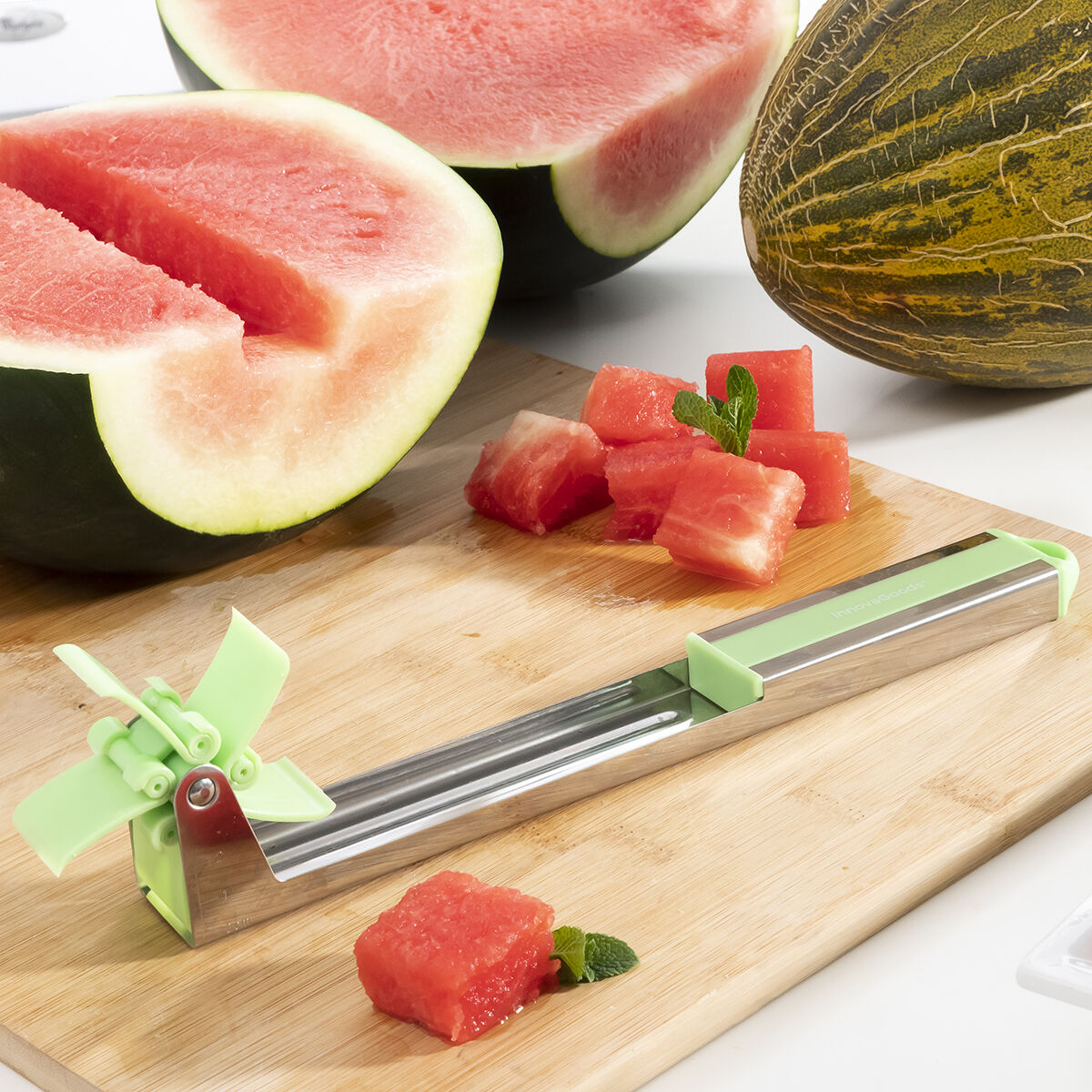 Wassermelonenscheiben auf einem Holzbrett, mit einem Wassermelonenschneider. Würfel und ganze Scheiben vorhanden.