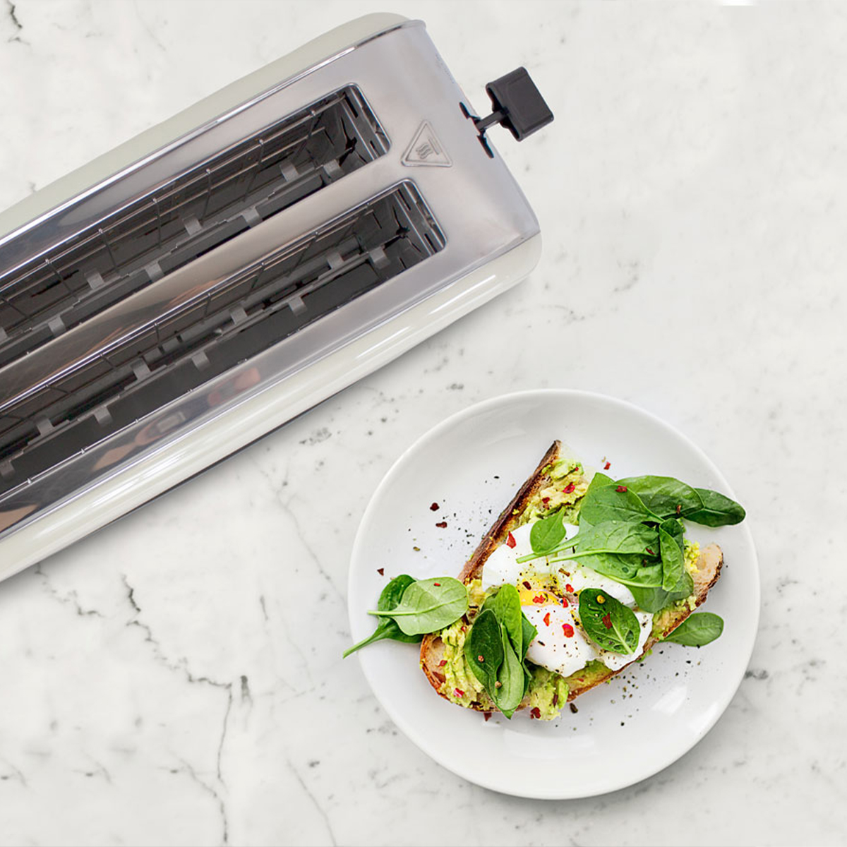 Toster i talerz z tostami z awokado, posypane szpinakiem, jajkiem w koszulce i płatkami czerwonej papryki.