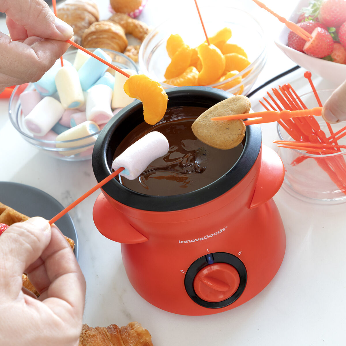 Personen tauchen Lebensmittel in einen roten Schokoladen-Fondue-Topf, umgeben von Snacks.