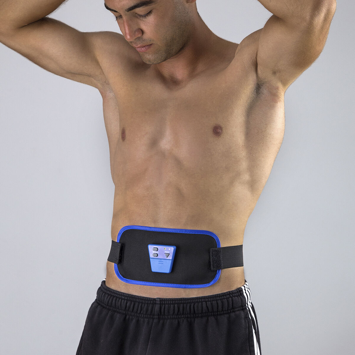 Un hombre sin camisa lleva un cinturón tonificador abdominal. Mira hacia abajo con las manos arriba.