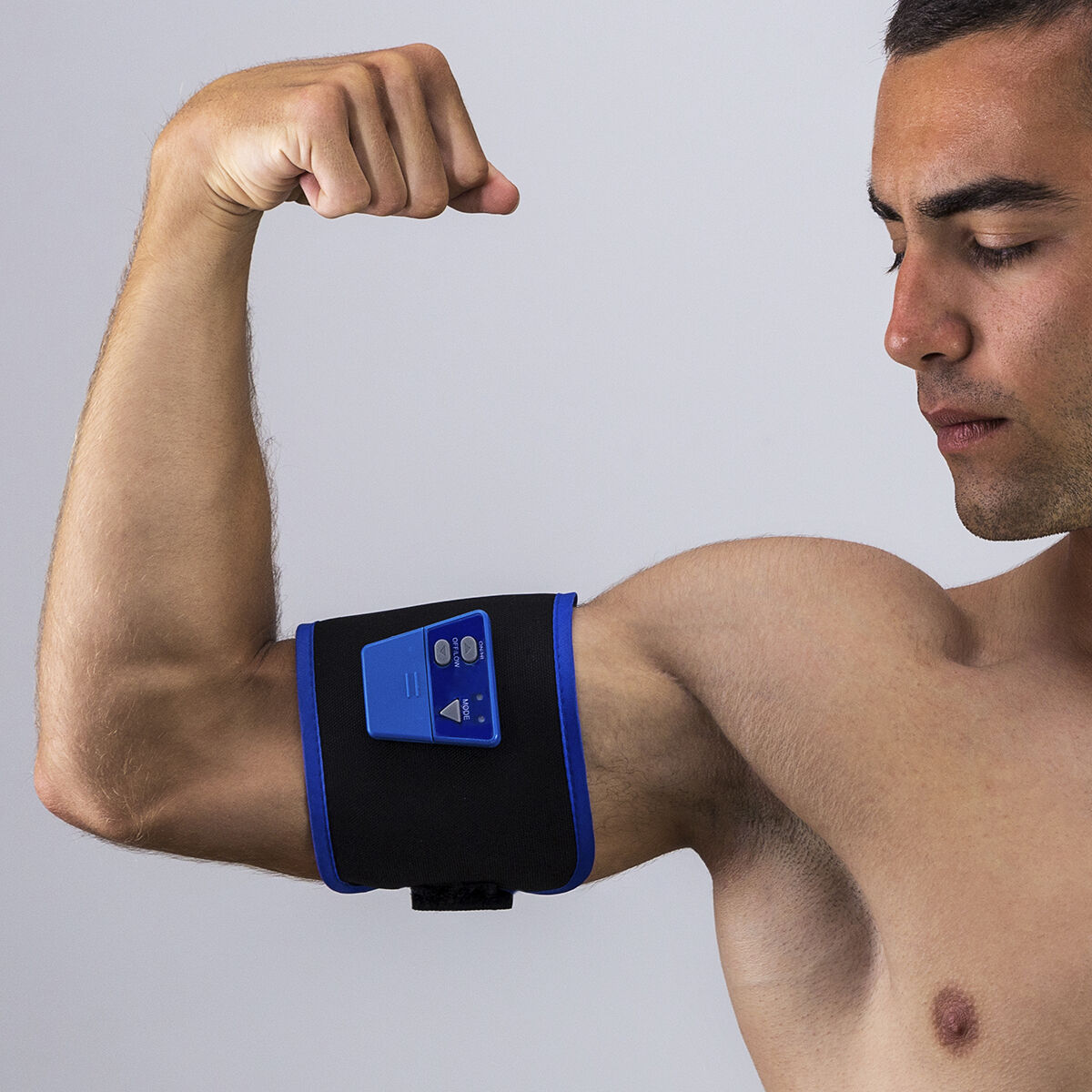 Un hombre con un estimulador muscular en el brazo. Está mirando hacia abajo.