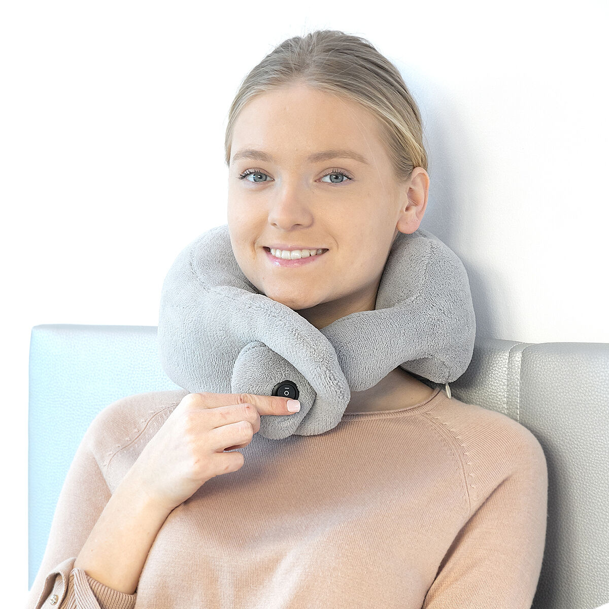 Mujer con almohada de cuello gris. Sonriendo y presionando un botón.
