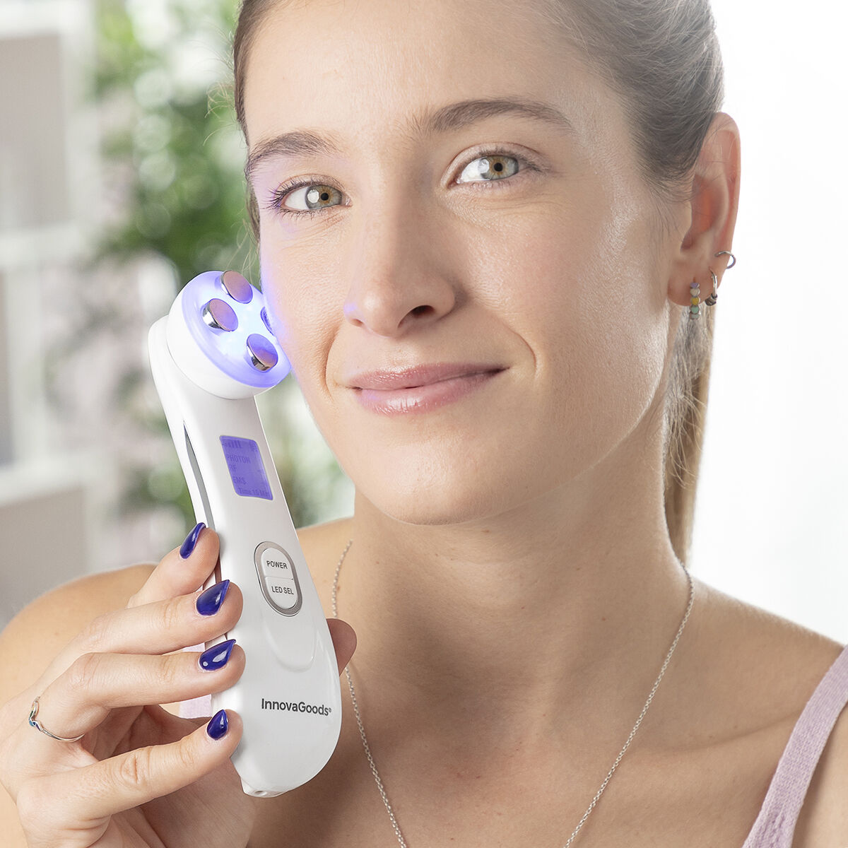 Una mujer sostiene un dispositivo de belleza blanco. Tiene luces azules y la marca InnovaGoods.