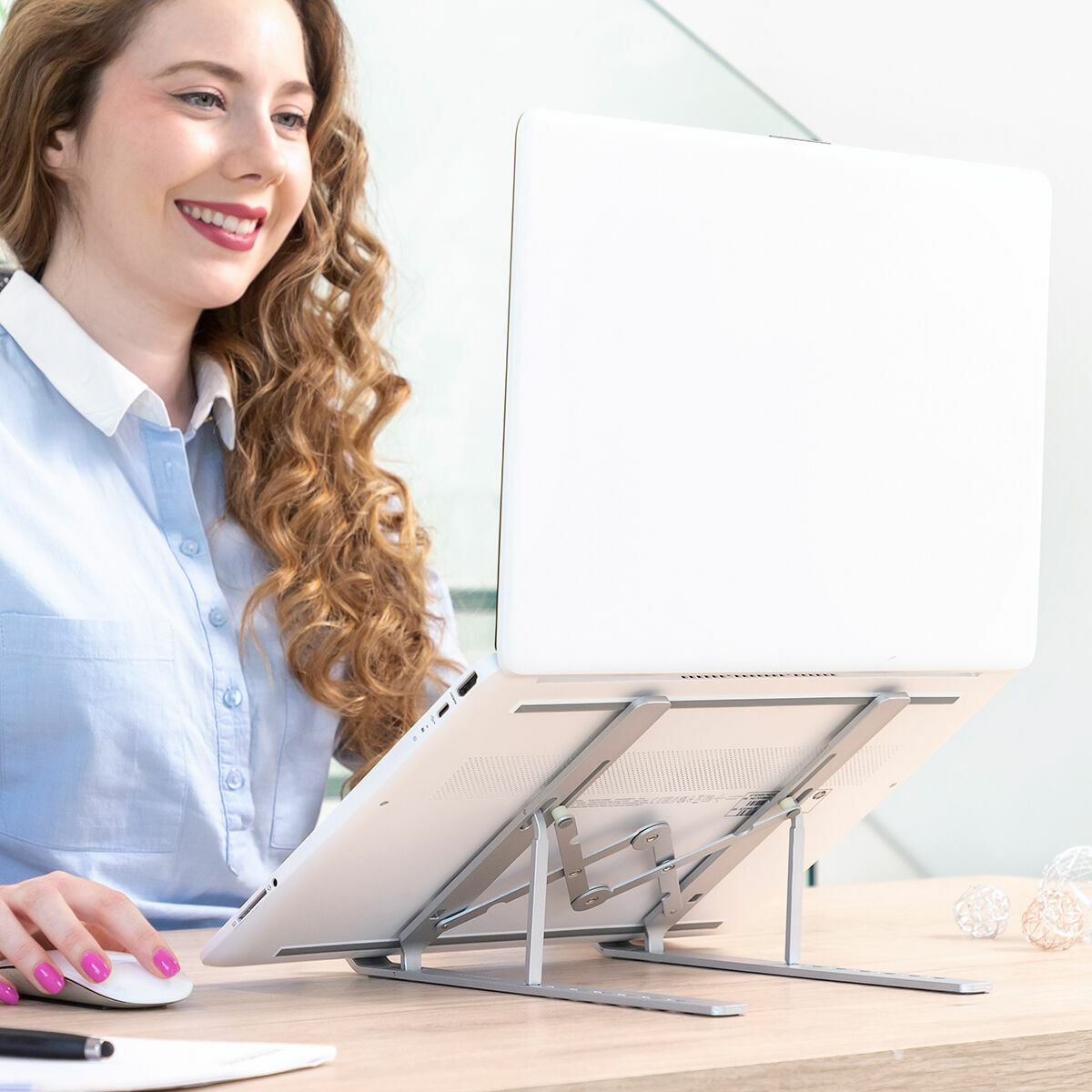 Eine Frau arbeitet an einem Laptop, der auf einem Laptopständer steht, und lächelt.