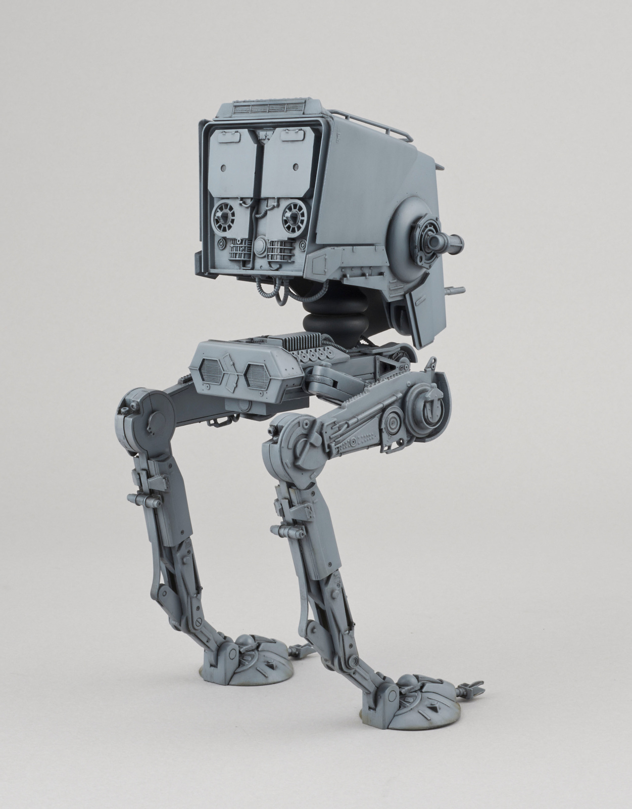 Un modèle de robot AT-ST gris, posé sur un fond clair, jambes écartées et tête en haut.