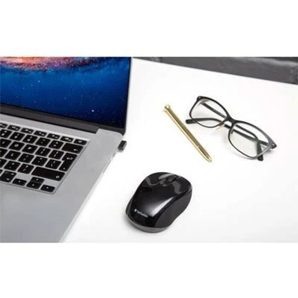 Laptop, czarna mysz, okulary i długopis na białej powierzchni. Laptop wyświetla scenę rozgwieżdżonego nieba na ekranie.