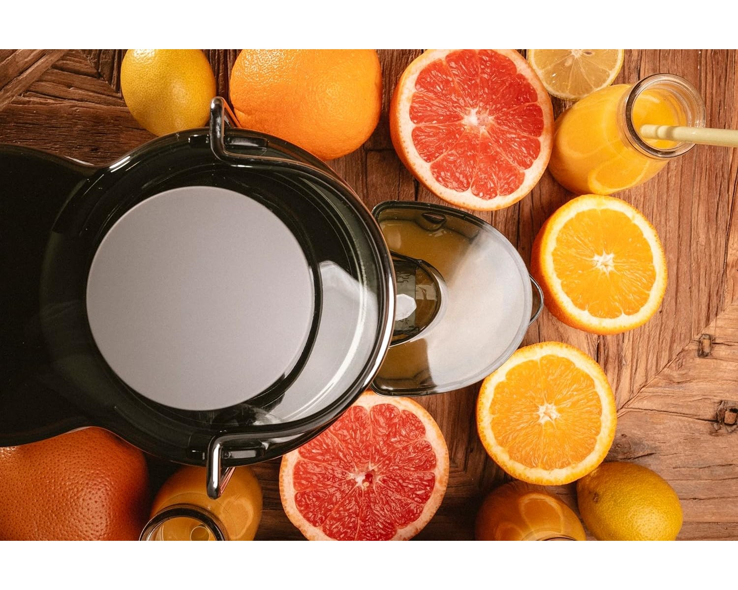 Entsafter mit Orangen, Grapefruit, Zitrone und Orangensaftflasche auf Holzoberfläche.