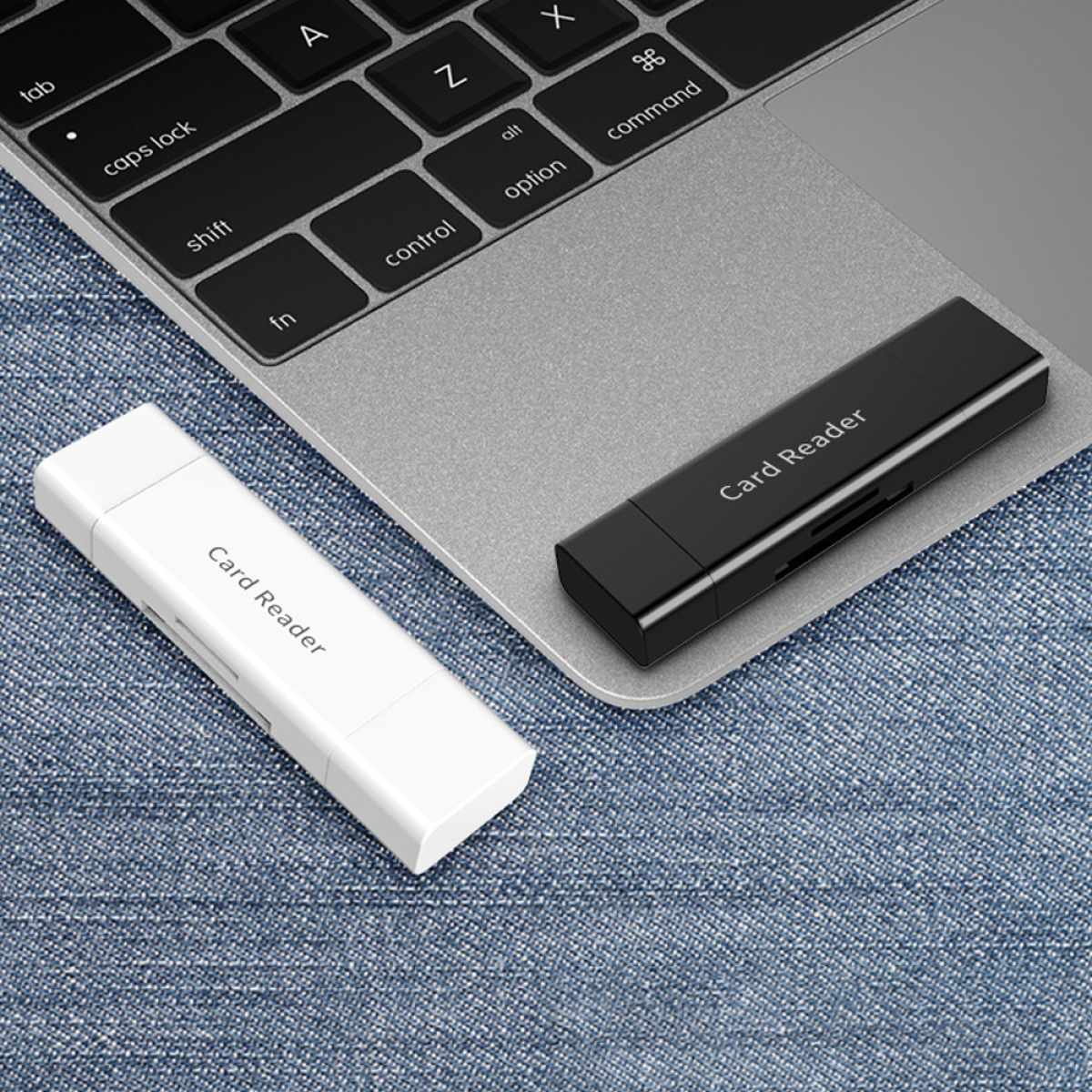 Zwei Kartenleser auf einem Laptop, einer weiß, einer schwarz. Jeans-Hintergrund.