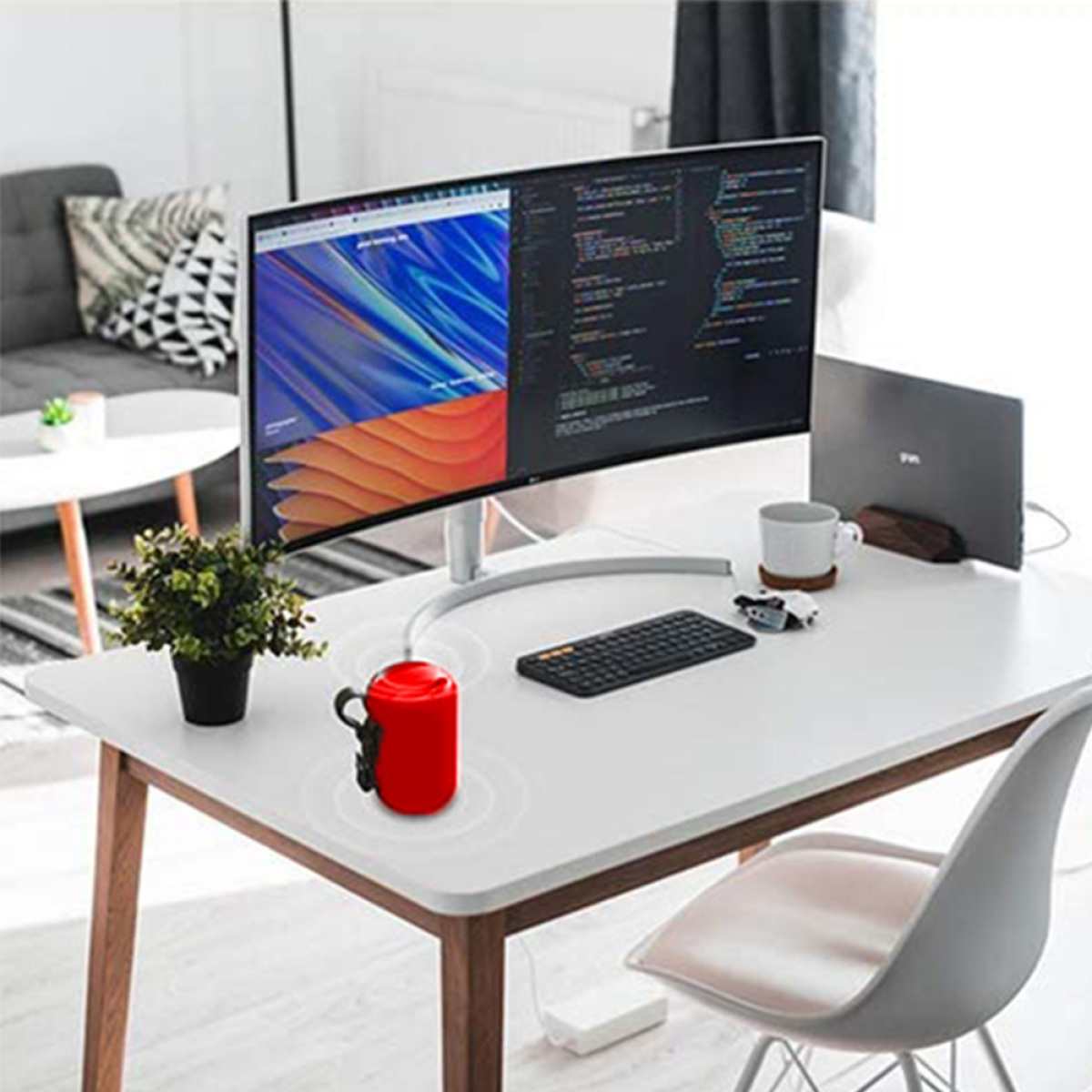 Ein roter Lautsprecher steht auf einem weißen Schreibtisch. Ein Monitor, eine Tastatur und ein Laptop sind ebenfalls vorhanden.