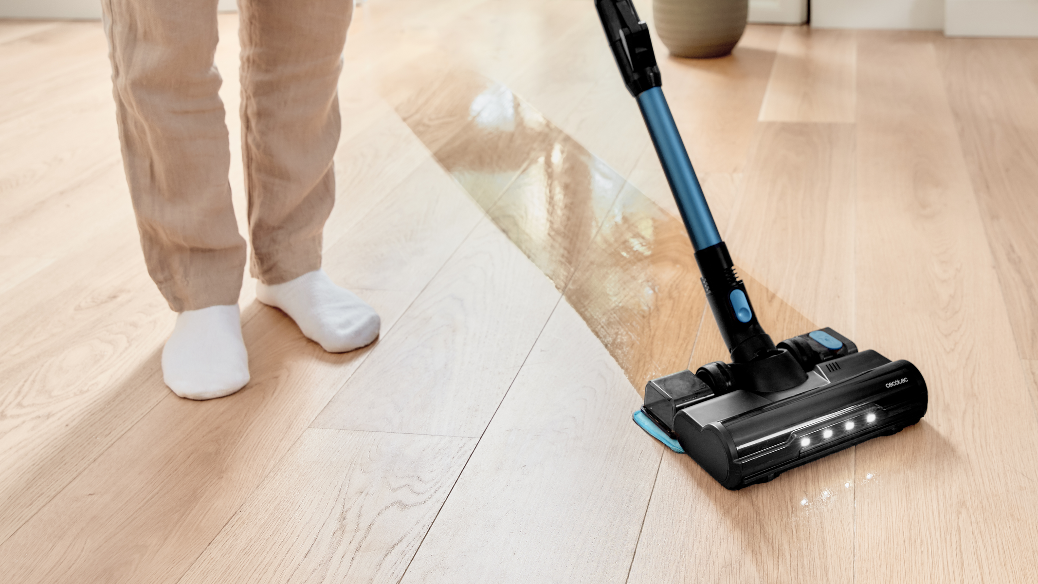 Persona con calzini che aspira pavimento in legno con aspirapolvere nero e blu.
