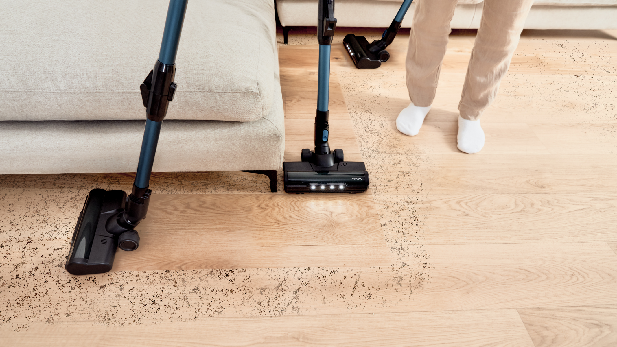 Due aspirapolveri puliscono un pavimento in legno. Uno è verticale, uno è portatile. Polvere visibile.