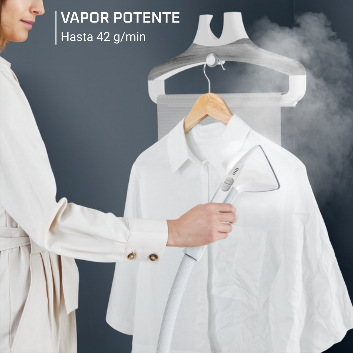 Donna che stira una camicia bianca con un vaporizzatore. Il vaporizzatore è su un appendiabiti. Sfondo grigio scuro.