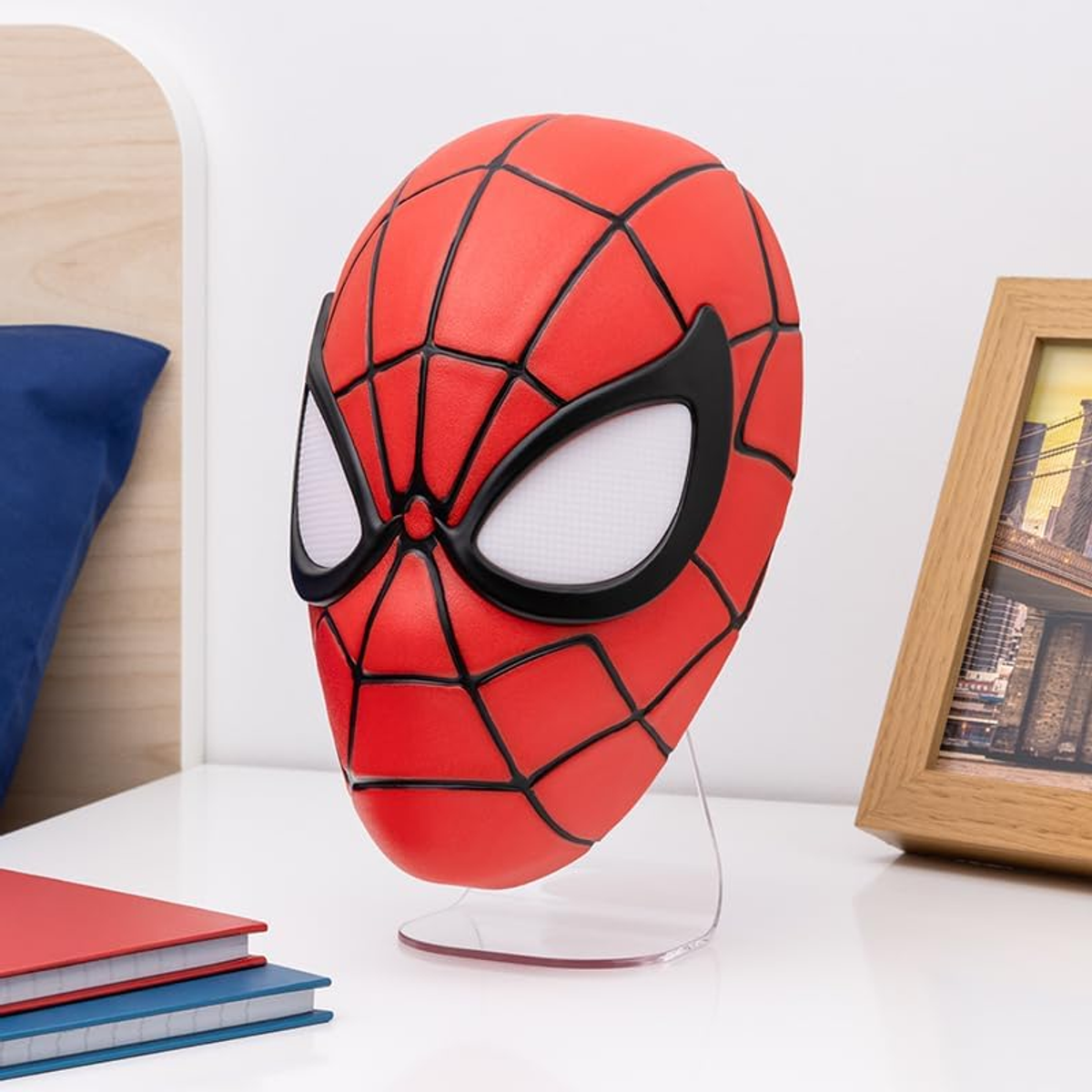 Maska Spider-Mana na stojaku na białym stole. Czerwona maska z czarnymi liniami i białymi oczami.