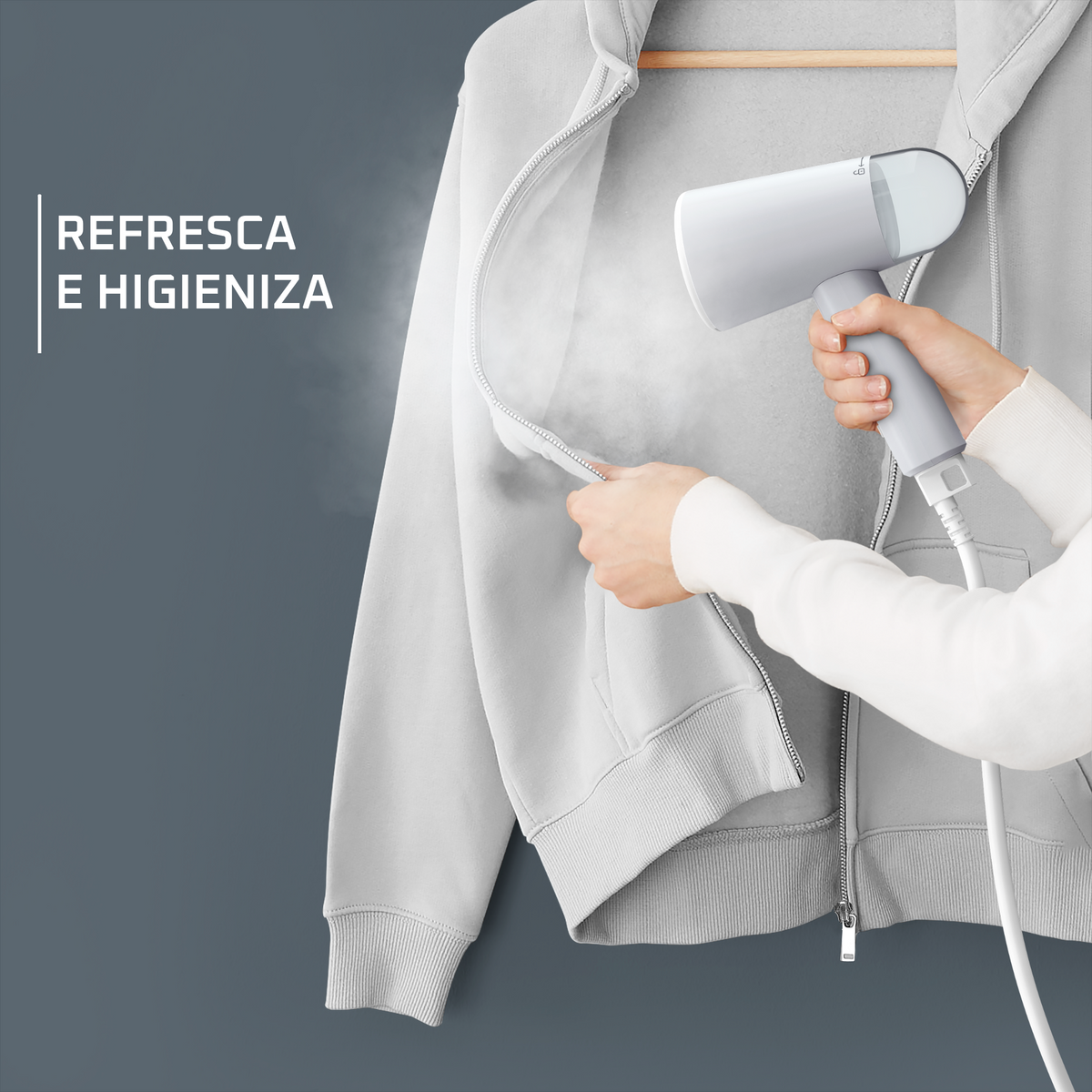 Una persona che stira una felpa grigia con uno steamer portatile. Testo: 'Rinfresca e igienizza'.