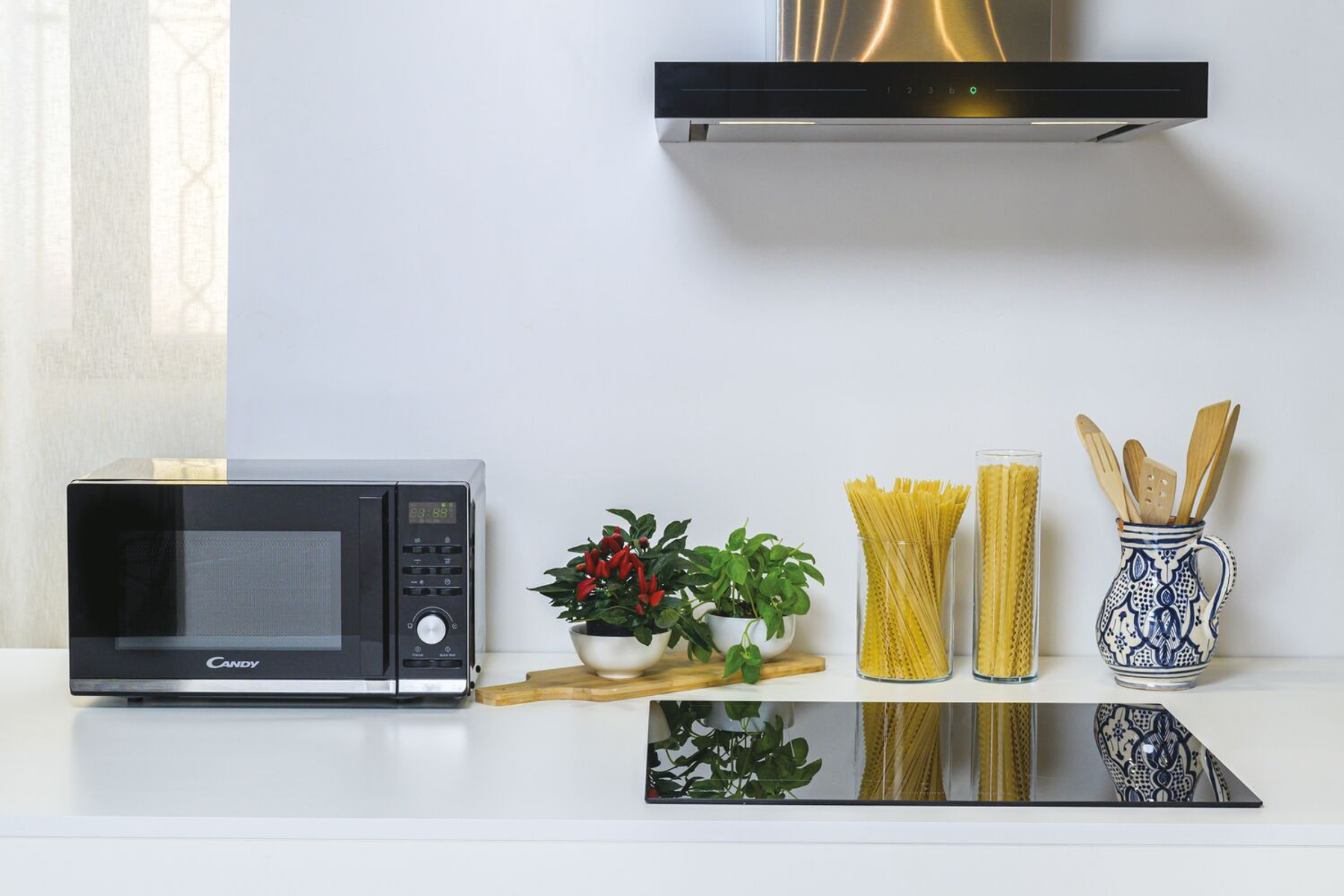 Scena kuchenna z kuchenką mikrofalową, makaronem, roślinami i białym blatem. Czarna kuchenka po lewej.