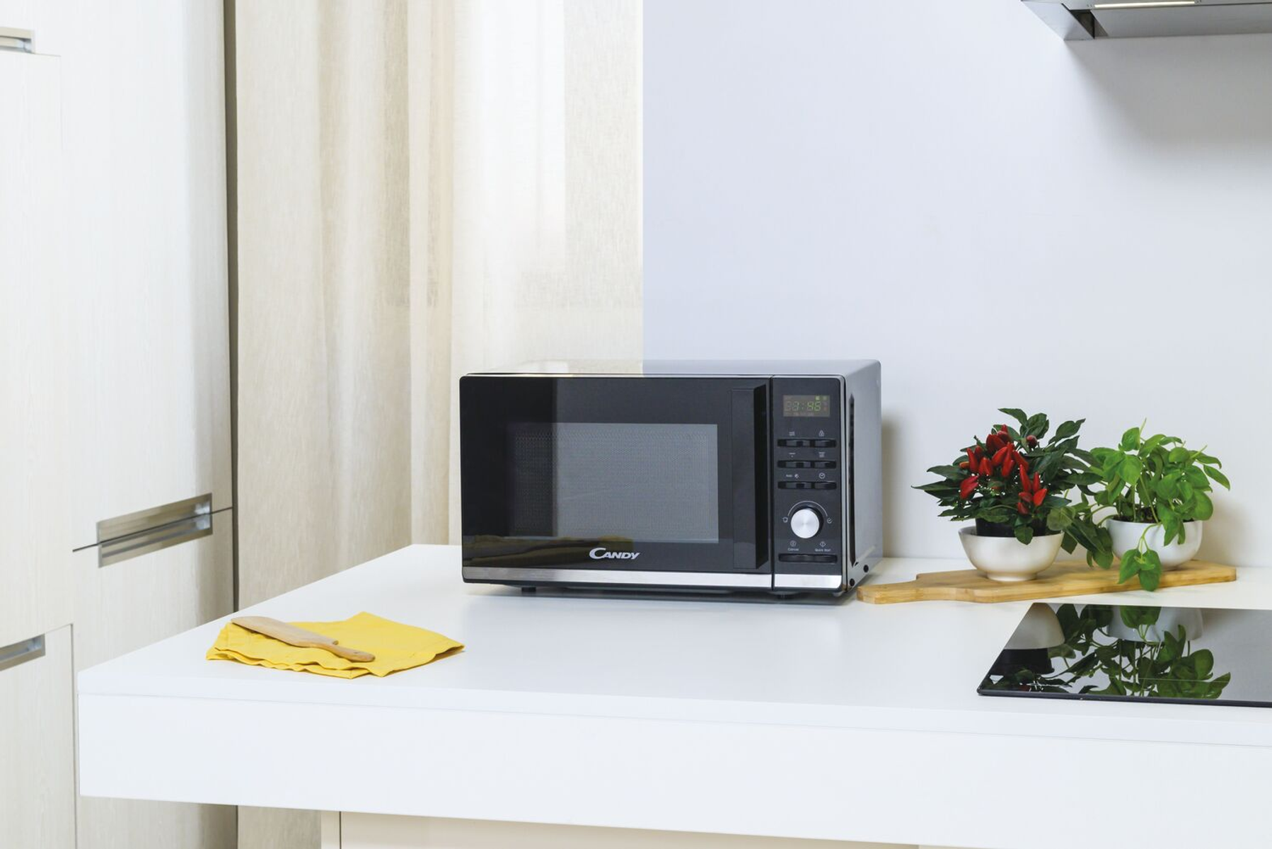 Kuchenka mikrofalowa na białym blacie z roślinami i drewnianą łyżką.
